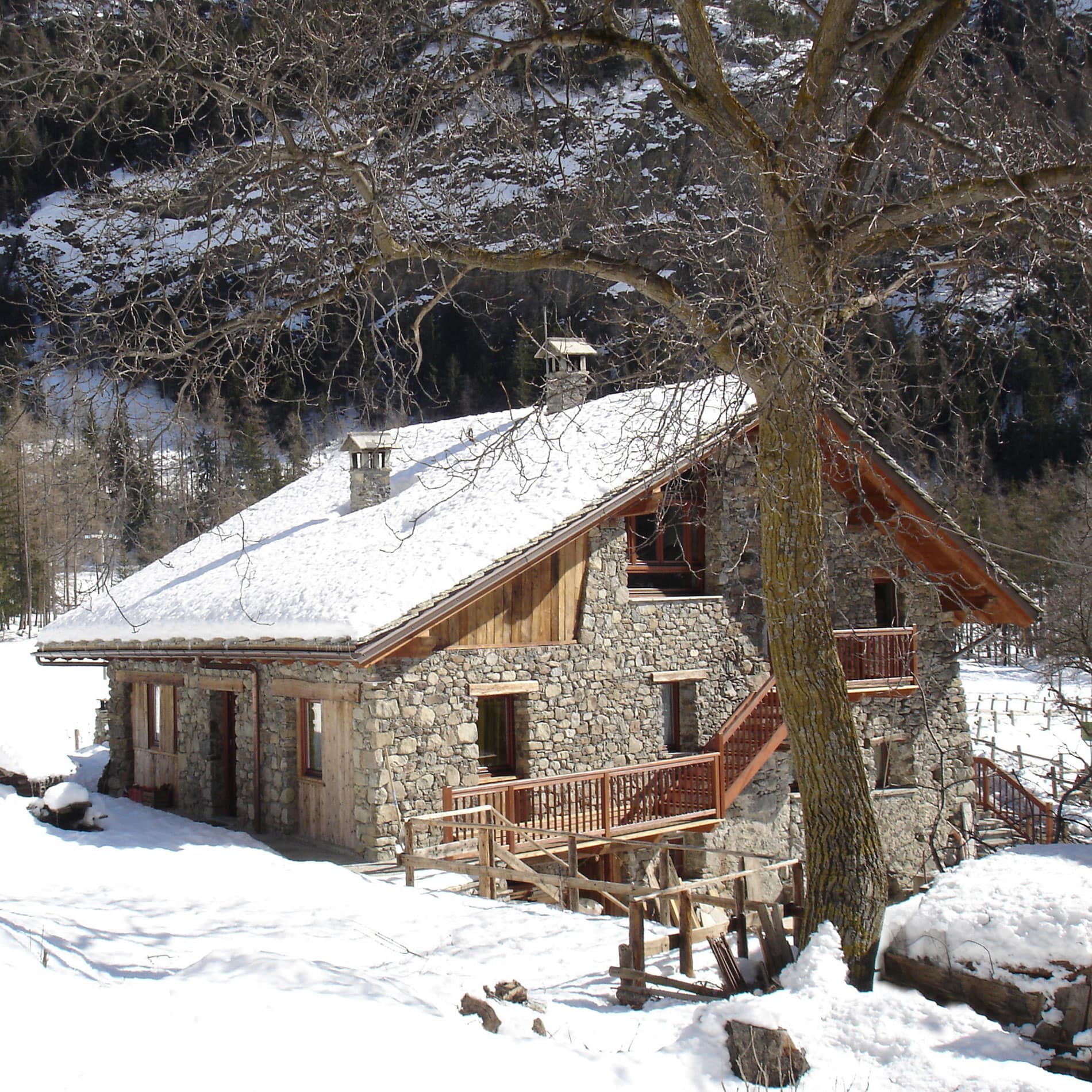 Groot chalet van steen en hout met houten trap langs het gebouw in een besneeuwde, bergachtige omgeving