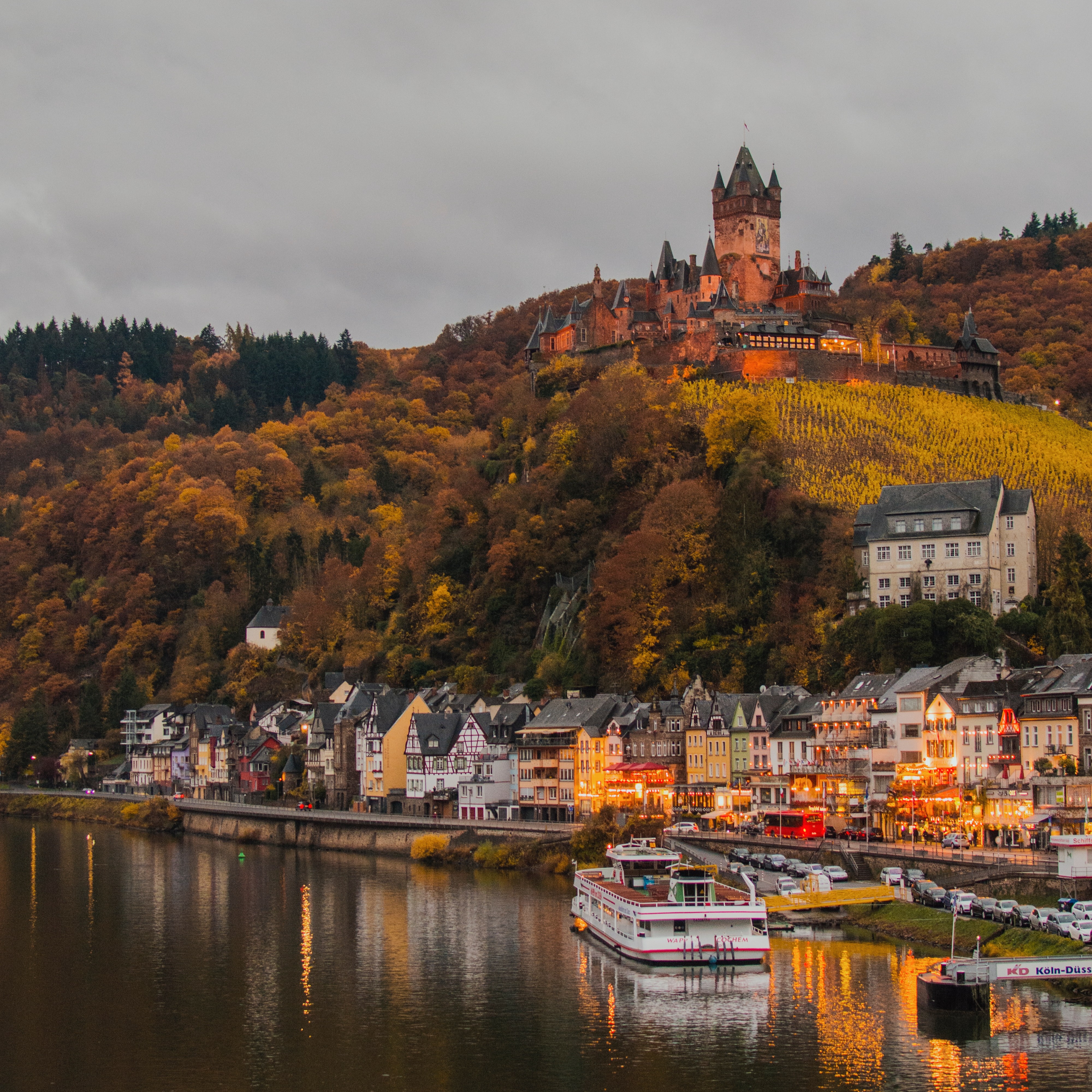 Cochem in de avond. De oever van de Moezel met gezellige terrasjes en het bergslot op de heuvel op de achtergrond. 