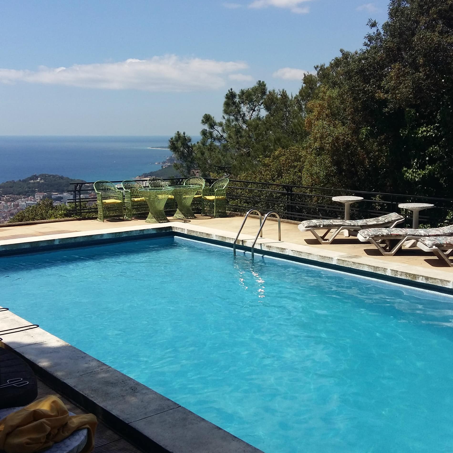 Een privézwembad met blauw water, zonnig terras, ligstoelen en zitje en weids uitzicht op de kust en de zee