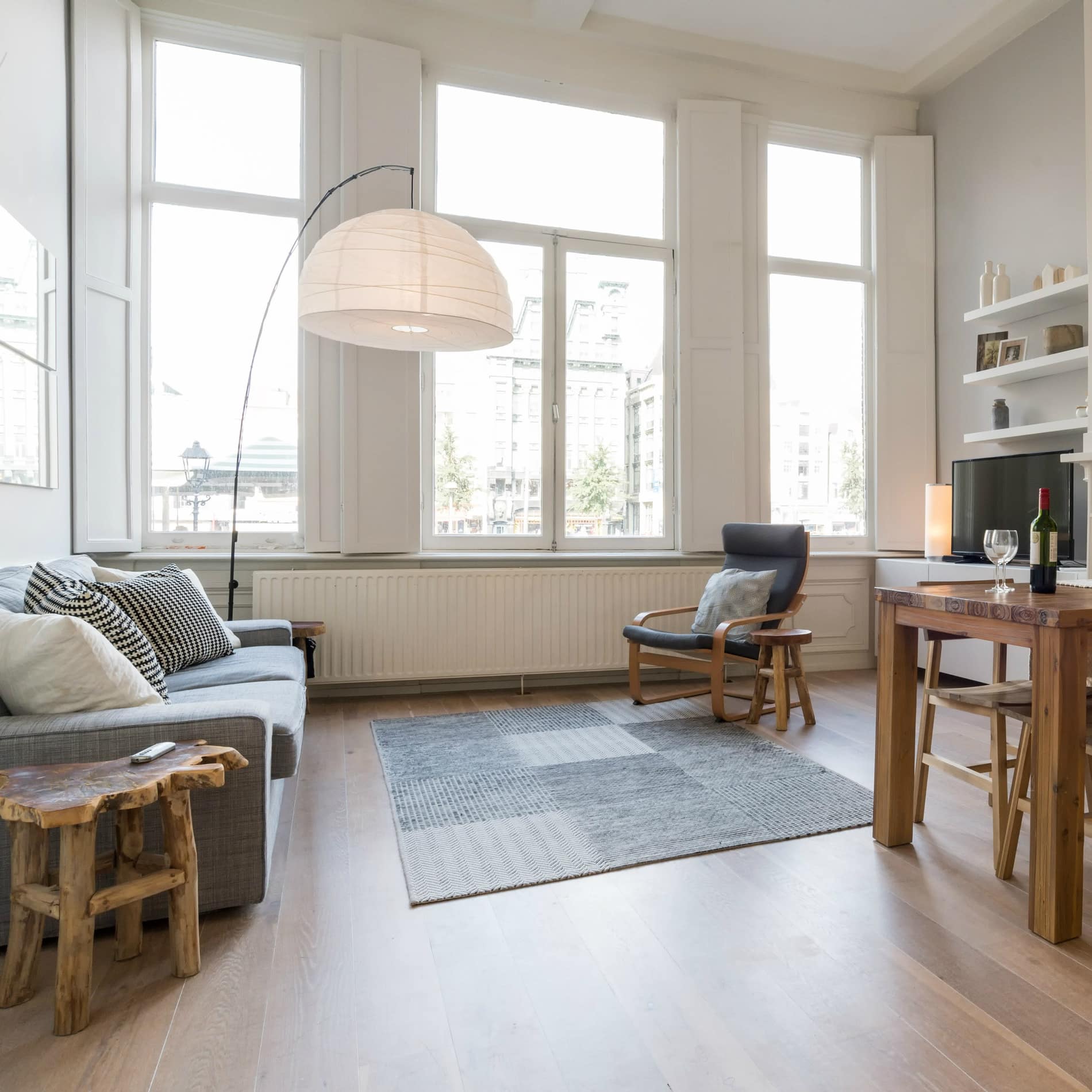 Lichte woonkamer met grote ramen, bank, luie stoel, eettafel en houten vloer