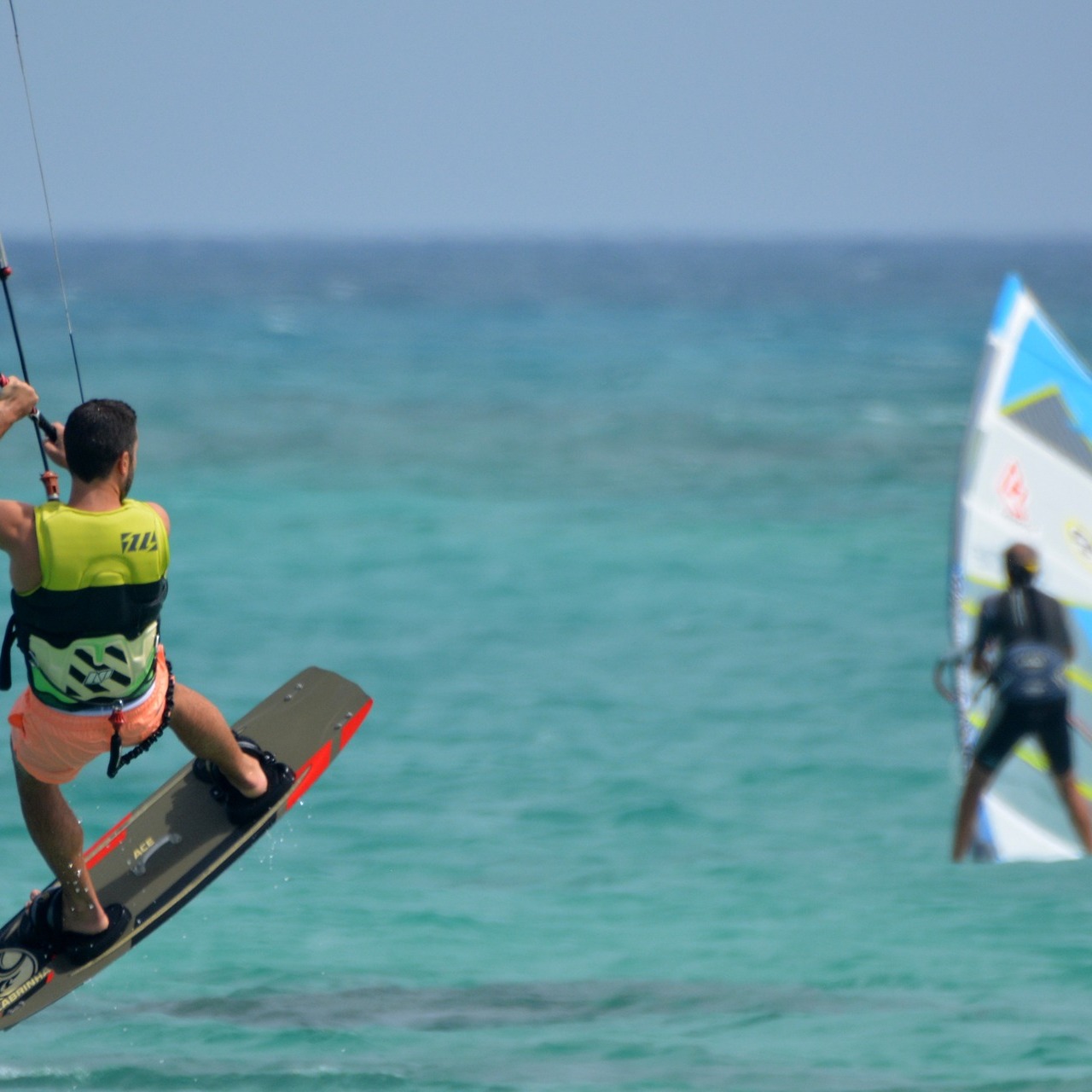 Twee watersportende mensen. Een kite surfer helder in de voorgrond en een windsurfer in de achtergrond.