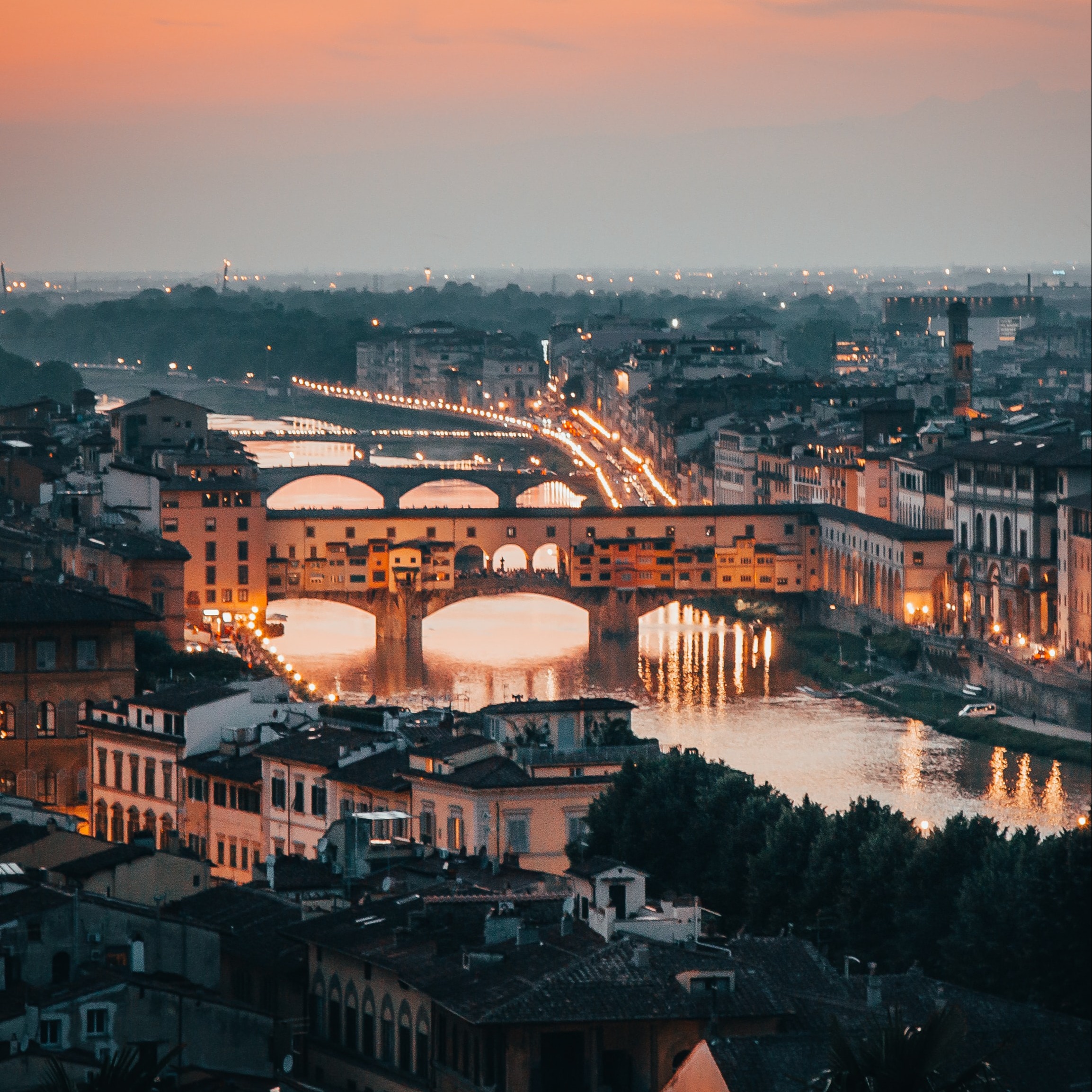 Een bij zonsondergang verlichte Ponte Vecchio over de rivier de Arno en uitzicht over een gezellig verlichte binnenstad van Florence. 