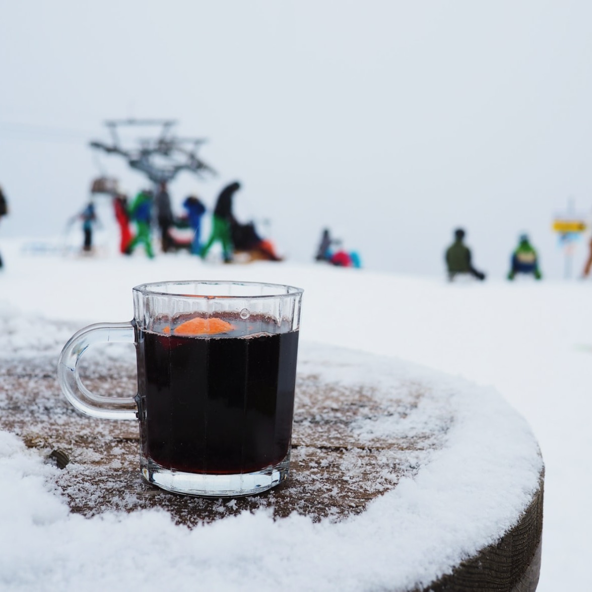 Een glas Glühwein op een besneeuwd tafeltje met op de achtergrond veel sleeënde kinderen op een helling