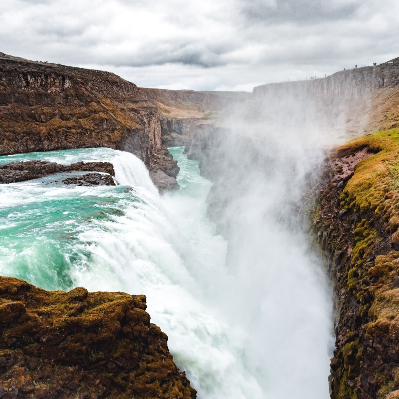 Uitzicht op een indrukwekkende waterval omringd door vulkanisch gesteente met IJslands mos.