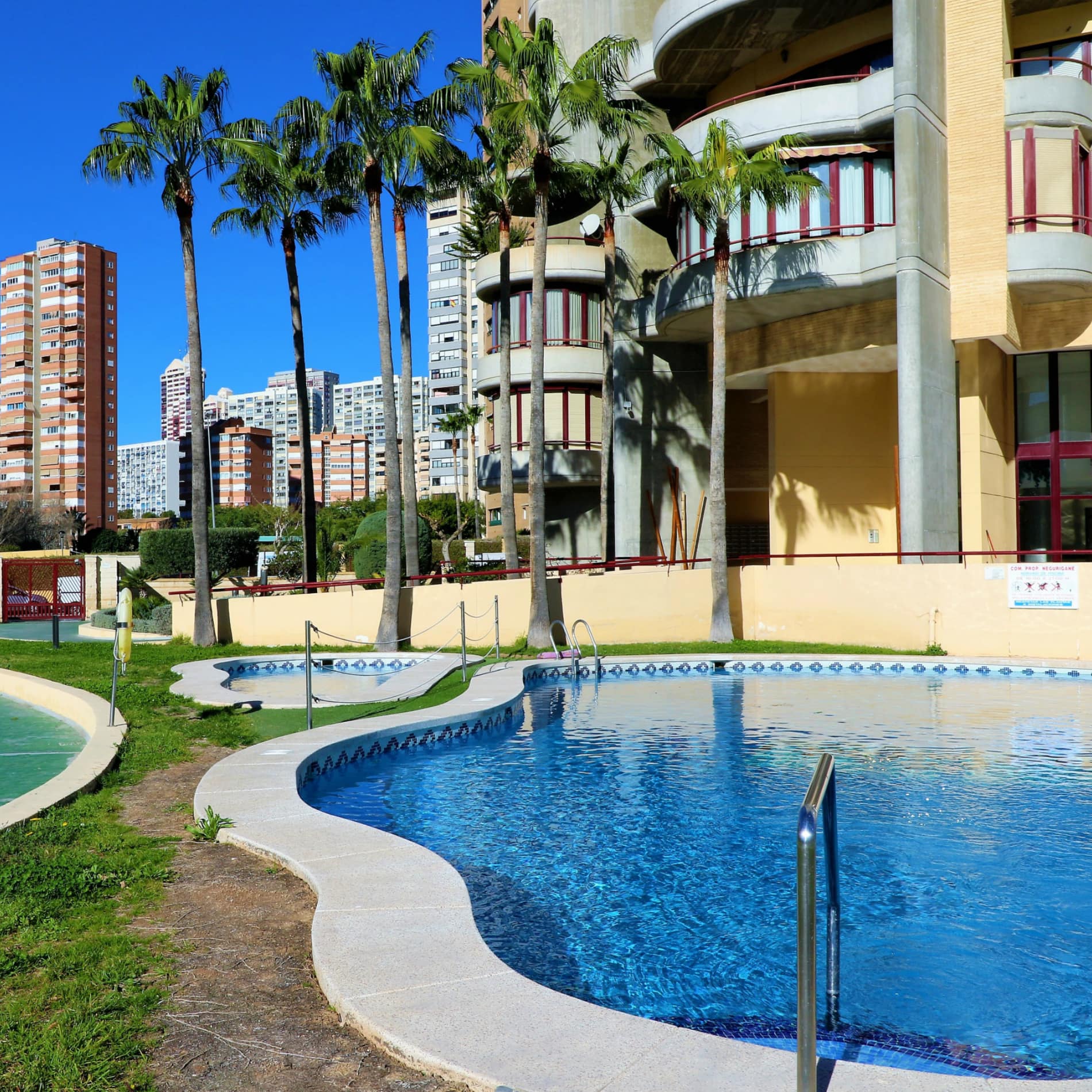 Zwembad met blauw water, palmbomen in de tuin van een appartementencomplex