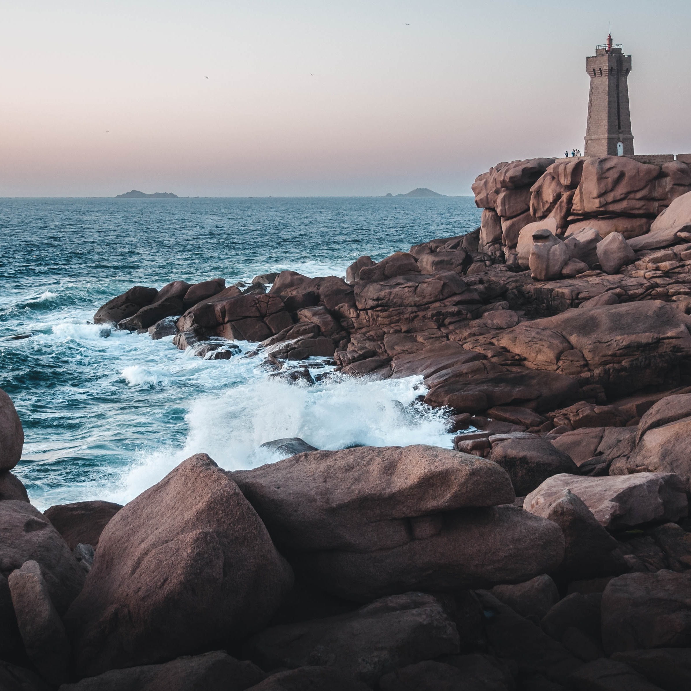 De uitzonderlijke roze granietkust in Bretagne met de heftige branding en een stenen vuurtoren op de rotsen. 