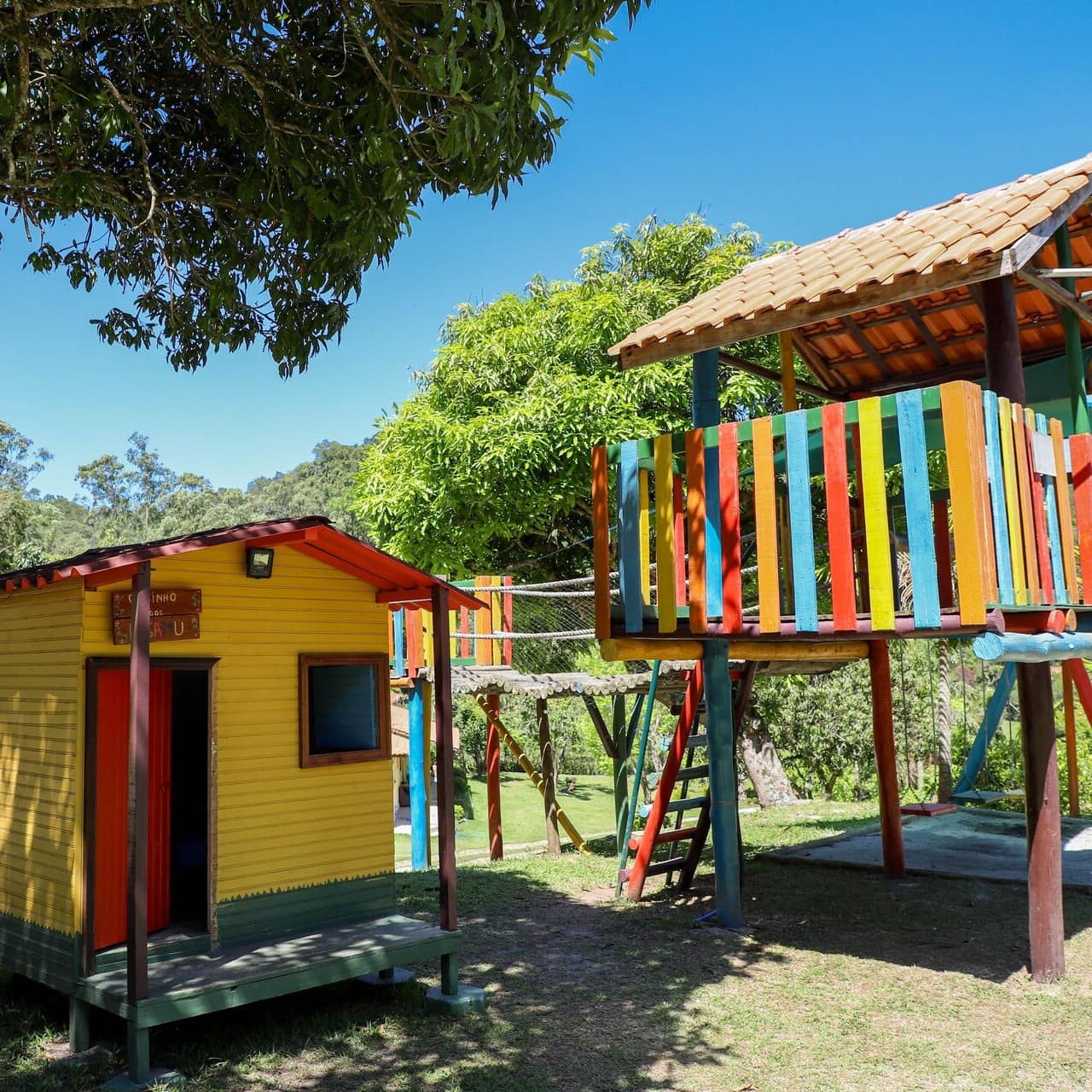 Parquinho com duas casinhas infantis de madeira coloridas, balanços e escorregador
