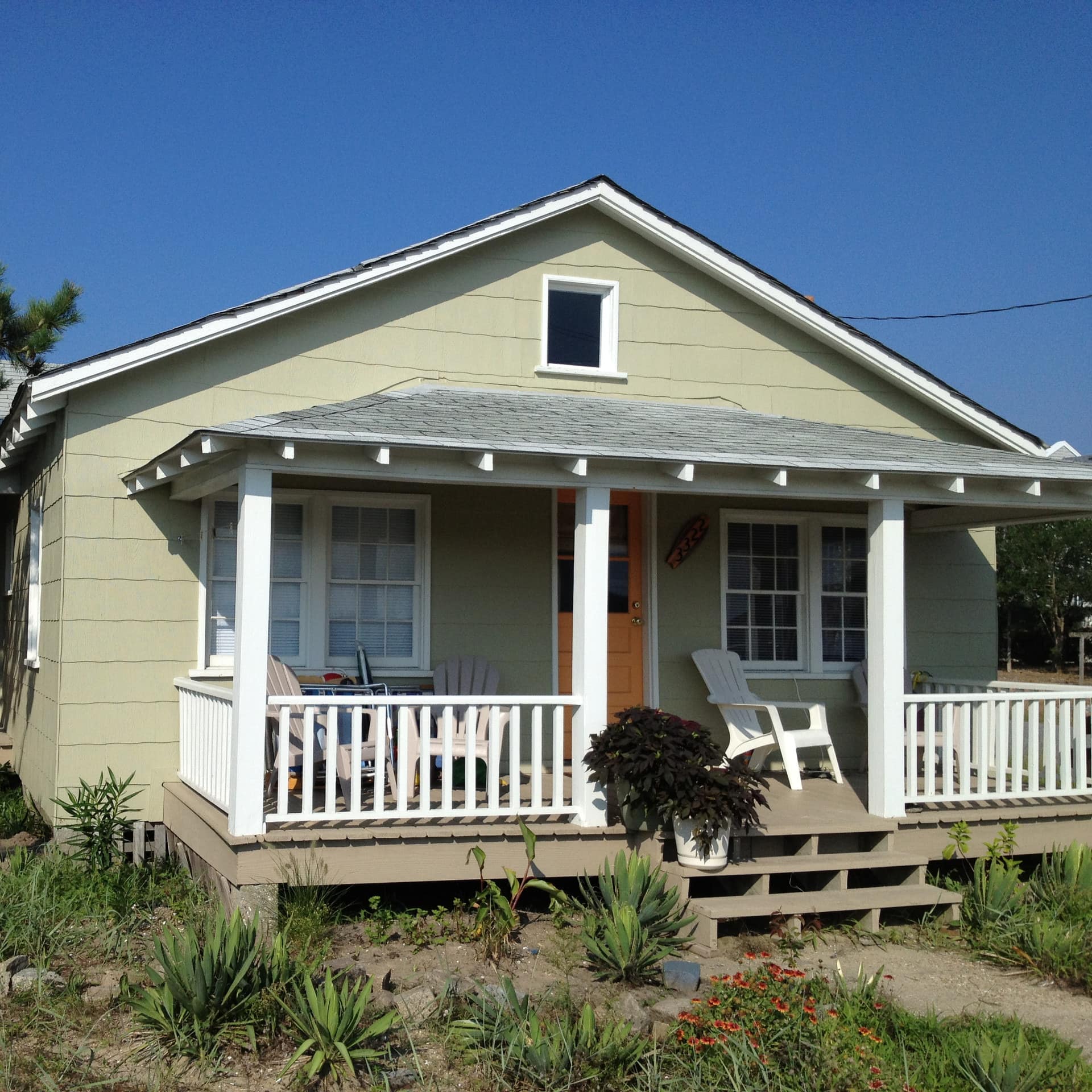 Exterior of a single story cabin with Adirondack chairs on the front porch and xeriscaped front yard