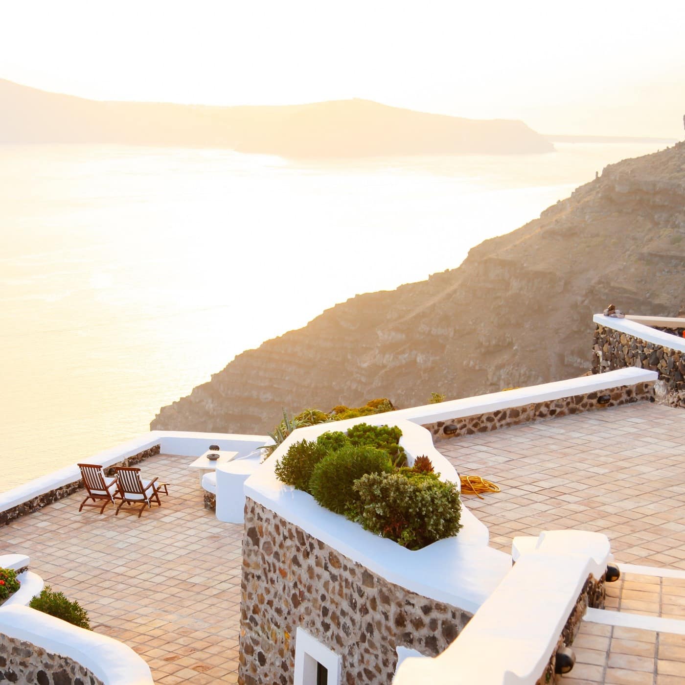 A luxurious, three-tiered patio with two deck chairs overlooks the Aegean Sea in Santorini