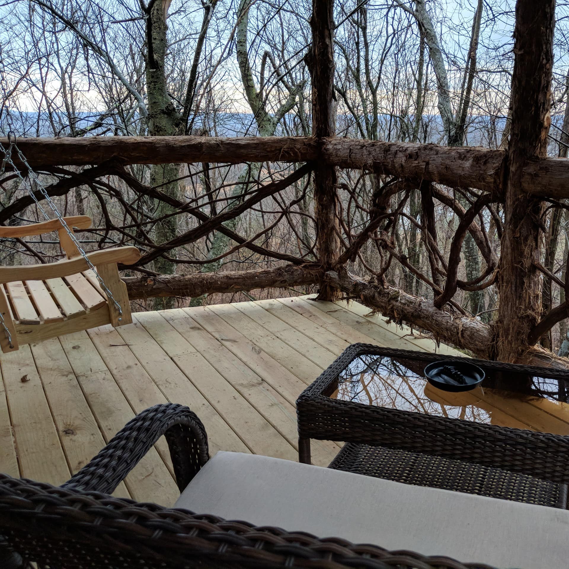 A deck with seating overlooks a forest in Arkansas from the side of a treehouse stay
