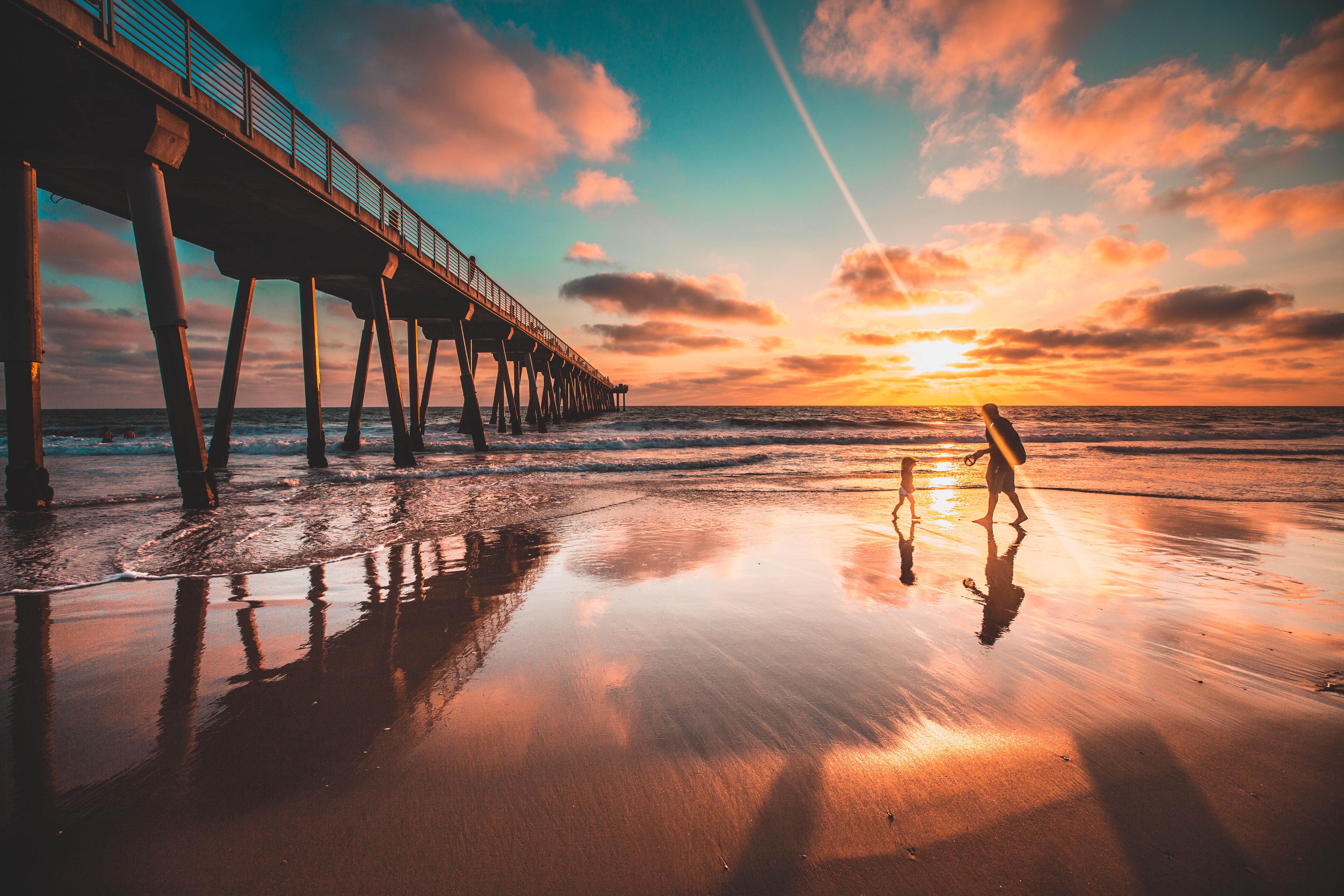 A silhouette of a father and daughter walking in the sunset underneath Hermosa Beach Pier