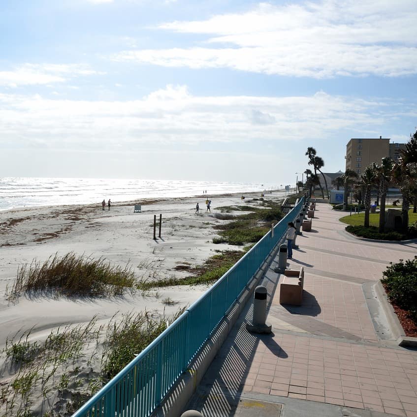 A leafy park runs by the sand dunes and waves of Daytona Beach