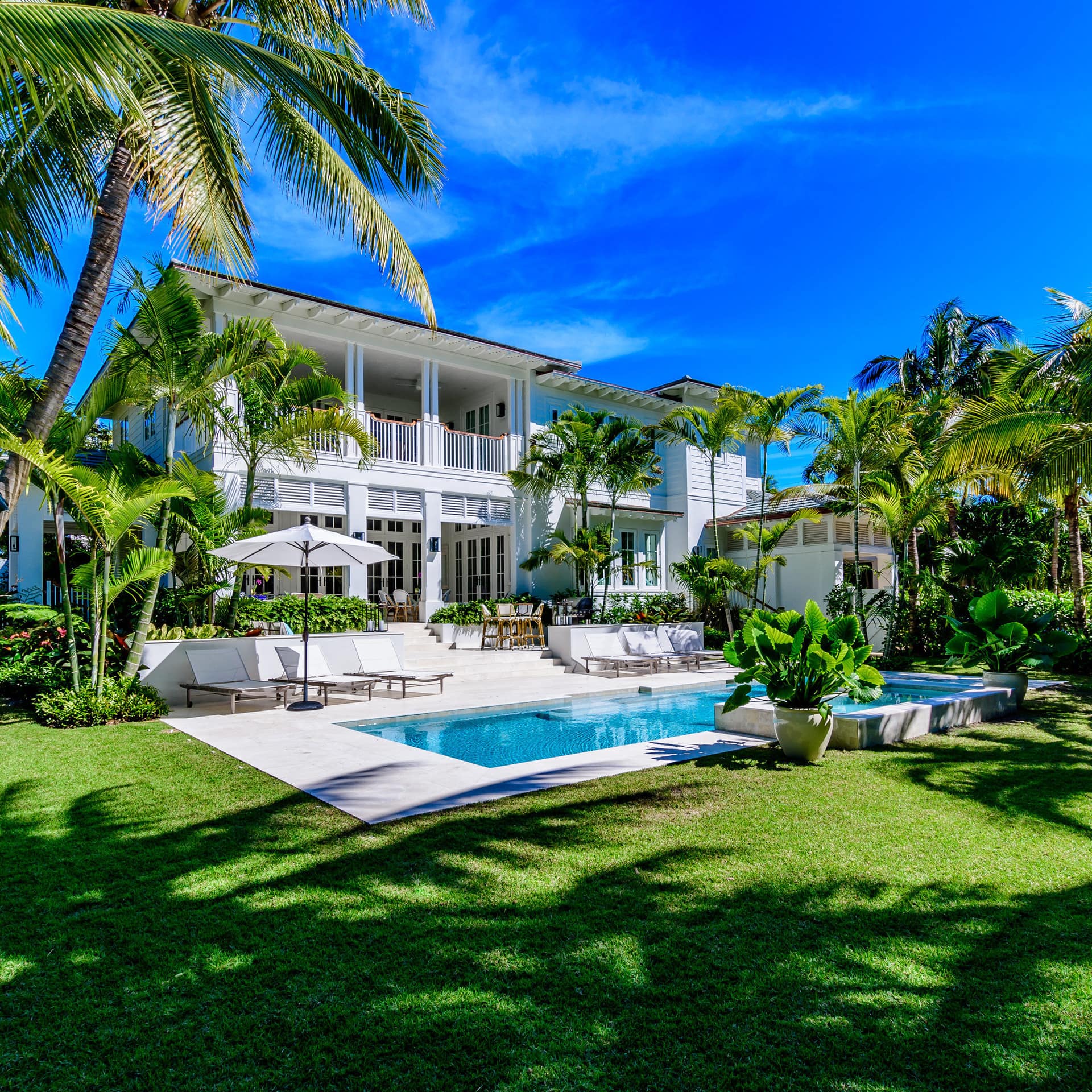 A large villa with a grassy garden and a pool surrounded by palm trees in Miami
