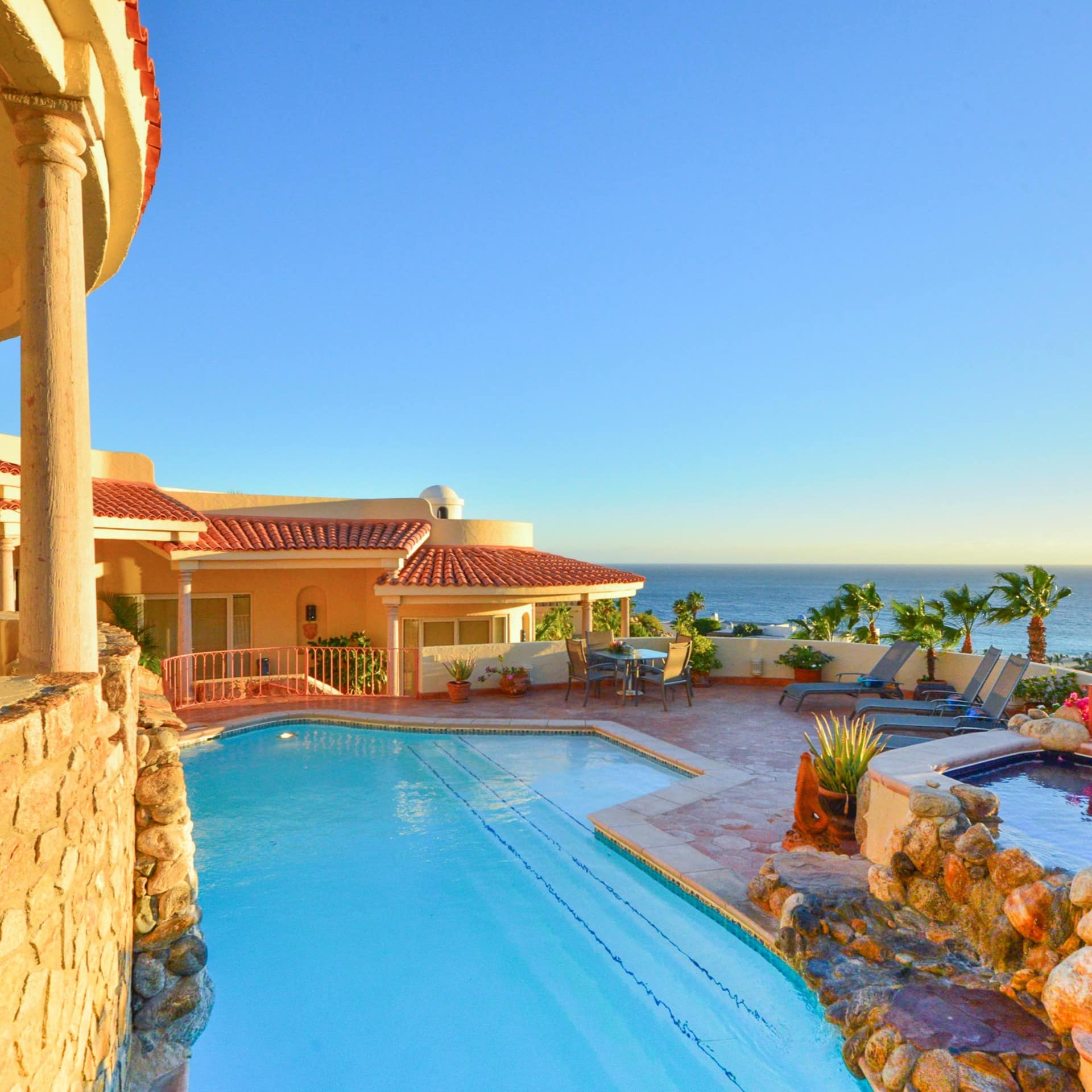 A sunny villa with a pool, sun beds, and seating area with beautiful ocean views
