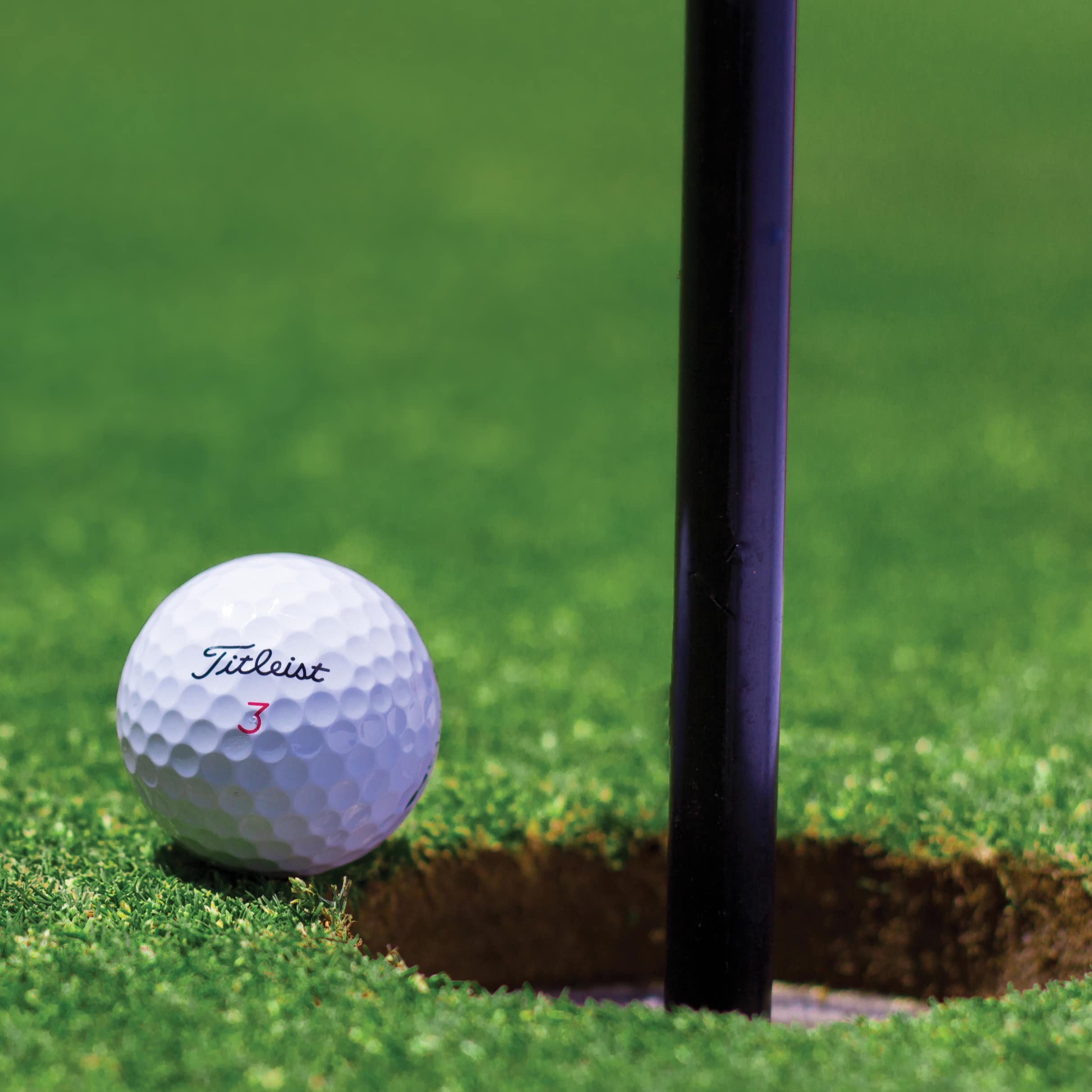 A golf ball poised at the edge of the hole.