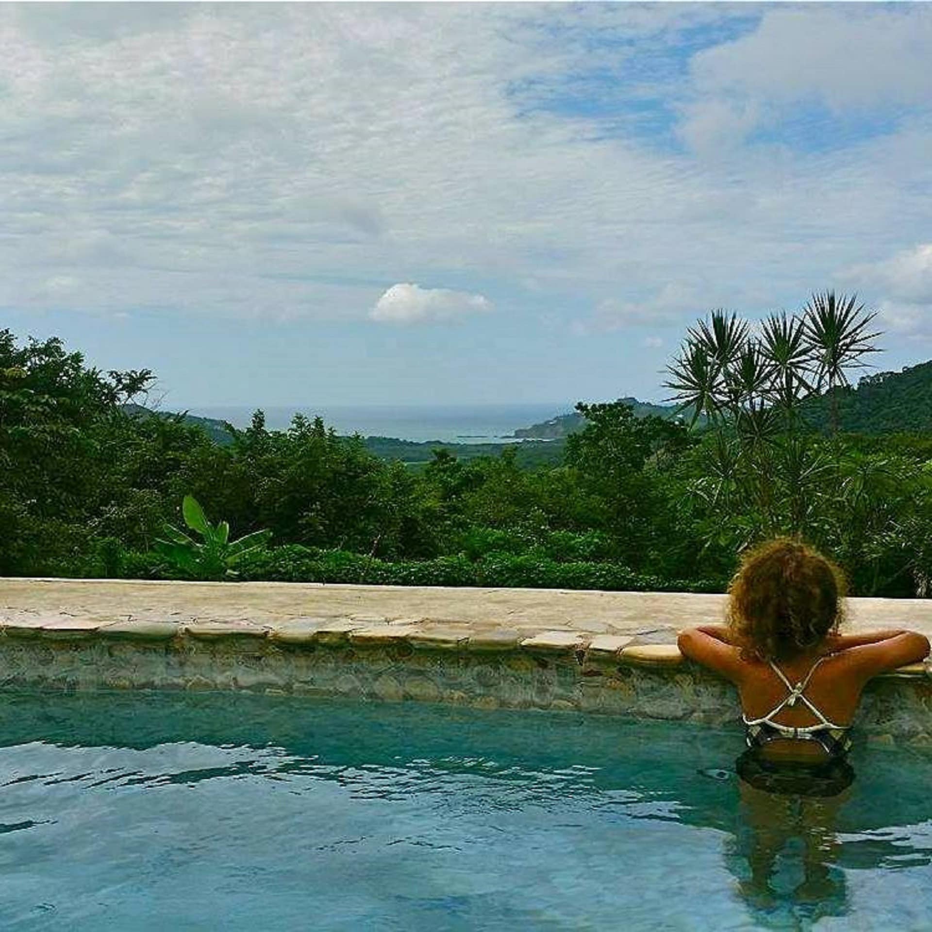 A girl in an outdoor swimming pool looking over lush greenery