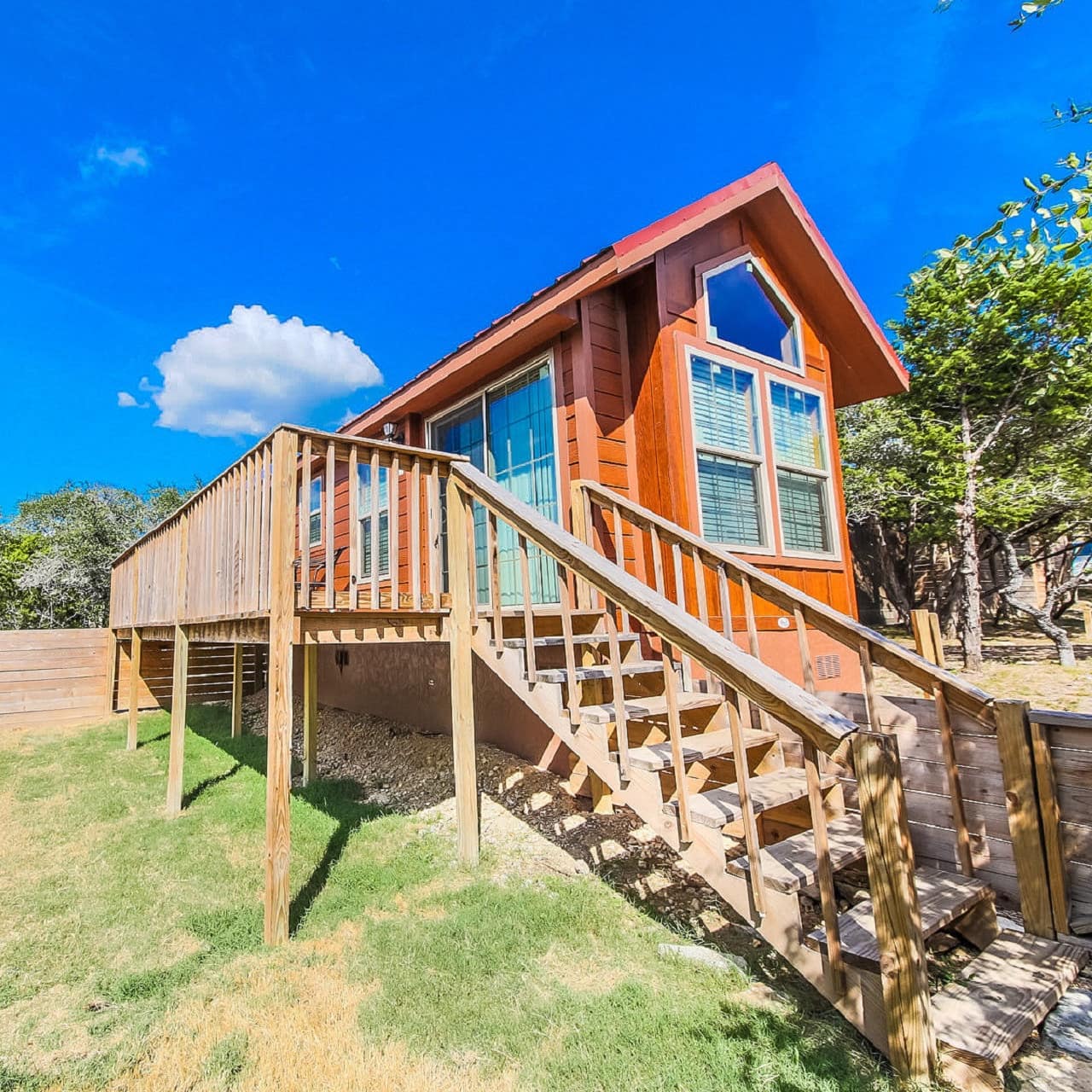 The sun drenches a wood-built cabin with a deck in the Texan Hill Country