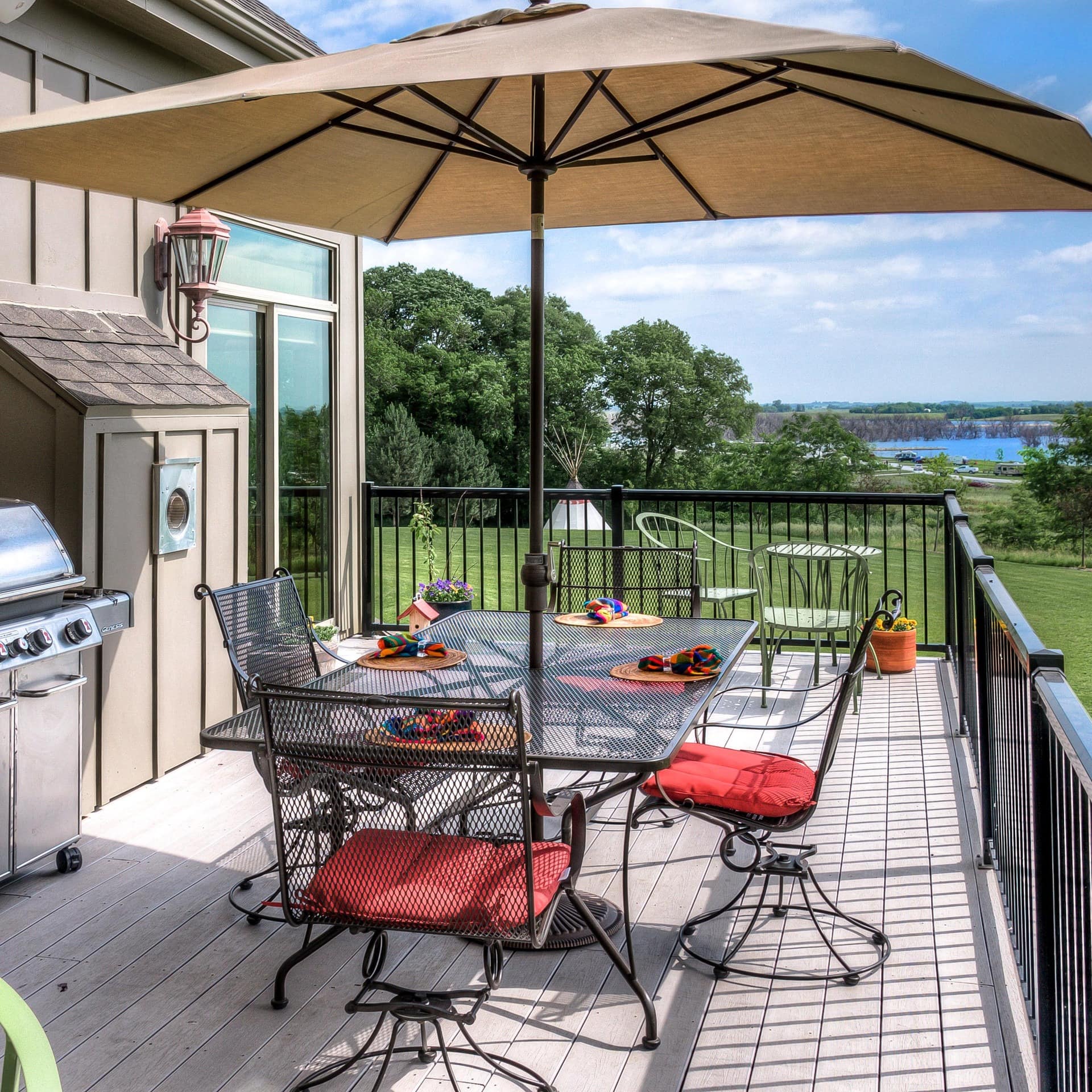 A grill and shaded tables and chairs on the deck of a luxury cabin with lake views