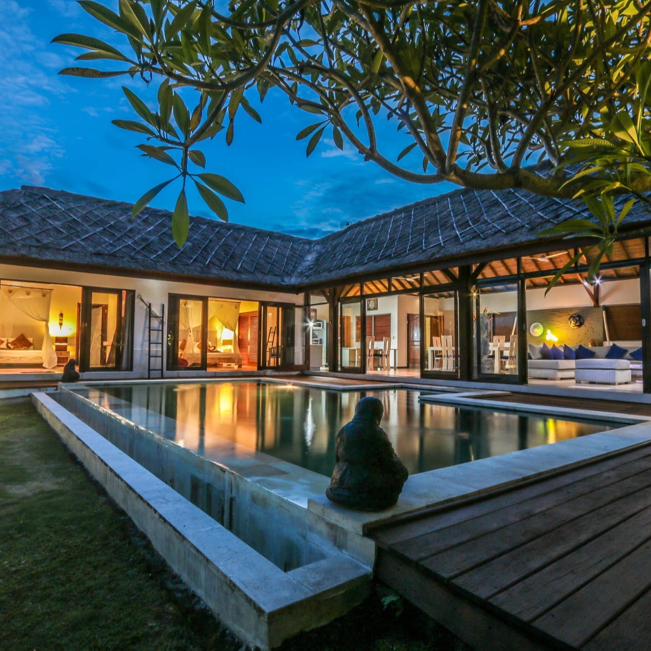 A luxury villa in Bali with big glass doors opening onto a deck area with a pool and traditional statues