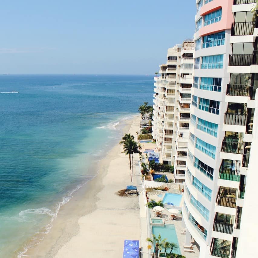A row of high-rise waterfront vacation rentals with pools stands by the ocean
