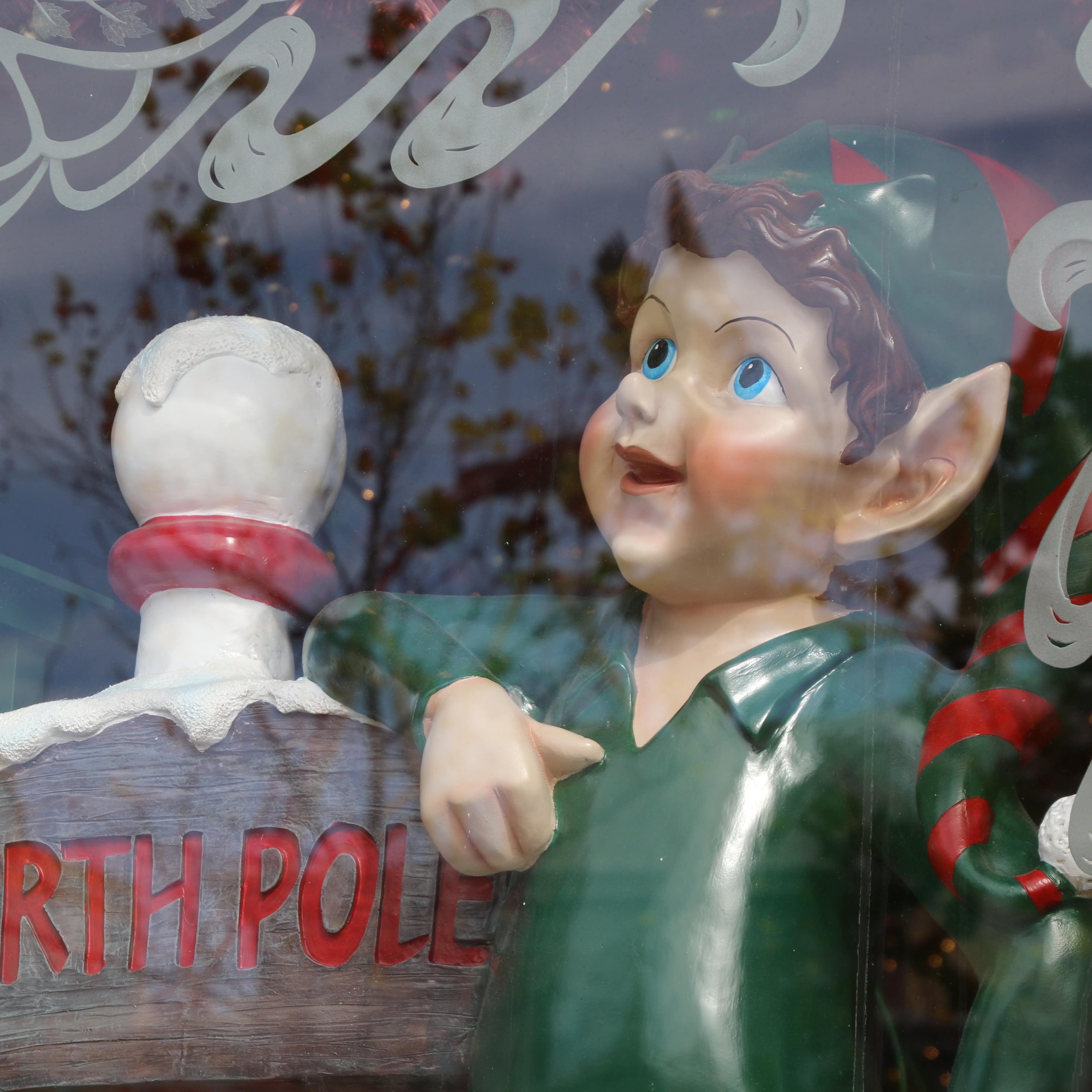 Elf in store window leaning on North Pole post