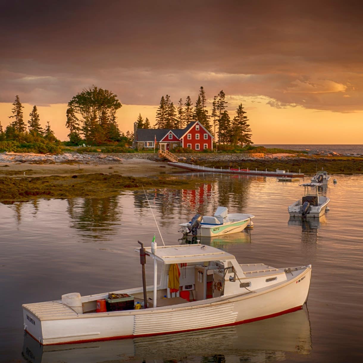 A red-painted house on the Maine coast with a jetty and boats out front