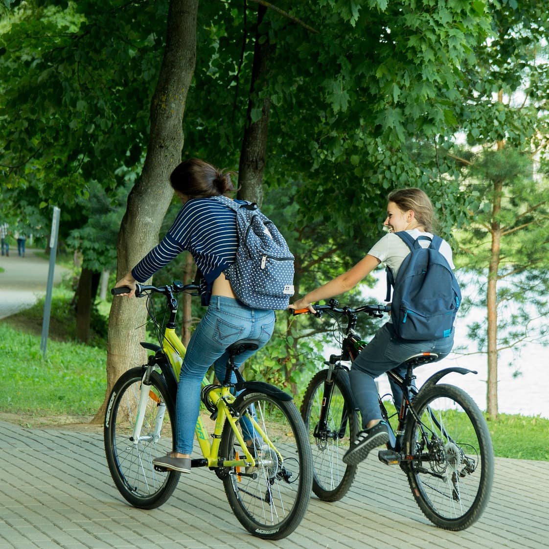 Two women ride their bikes on a park trail.