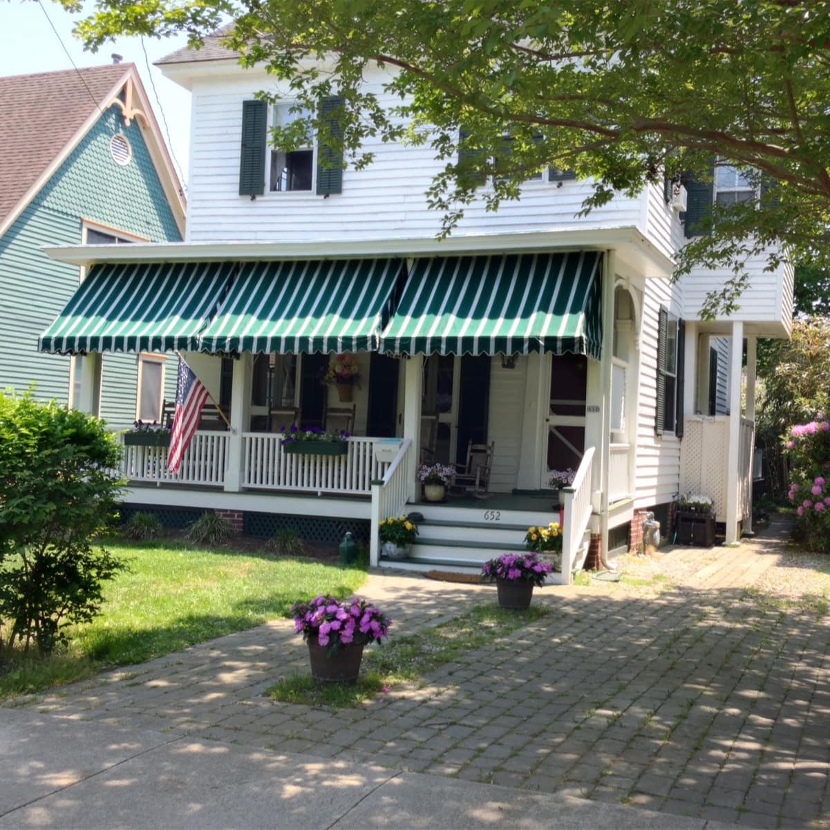 A shaded porch that's filled with magenta flowers fronts a white Cape May cottage