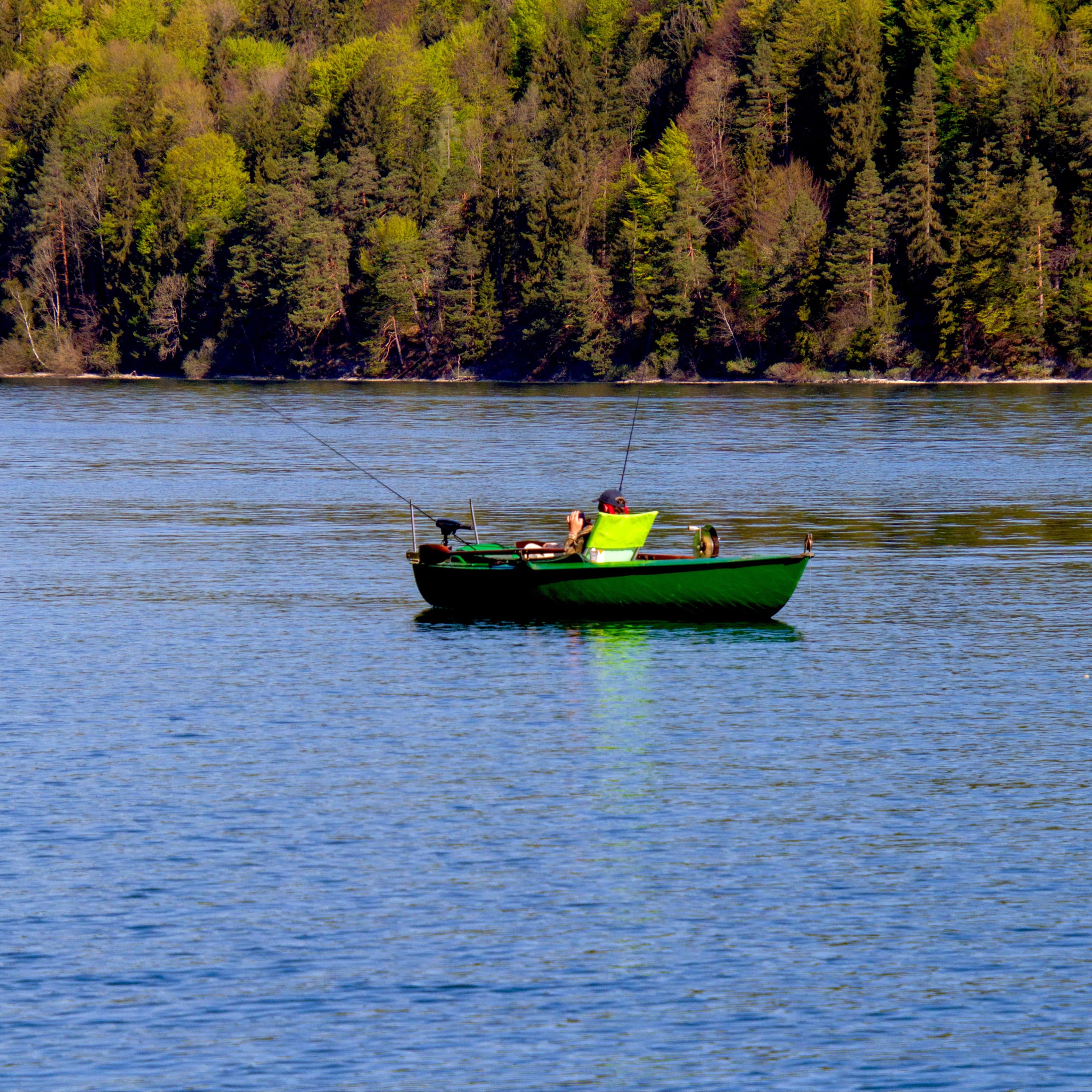 Man fishing in a fishing boat in the middle of a lake with trees by the shore