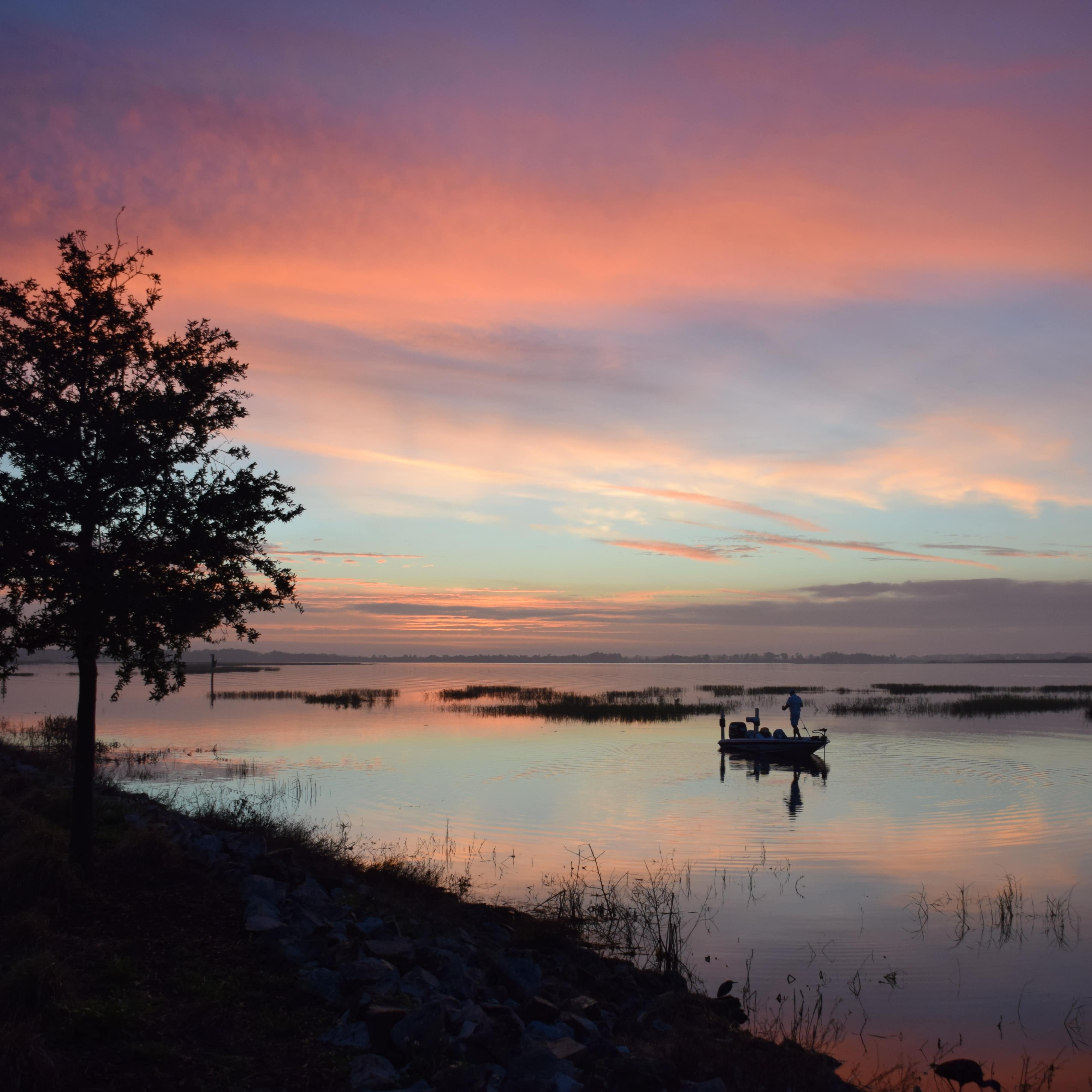 Small boat with a silhouette of a man bass fishing at sunrise on Lake Toho