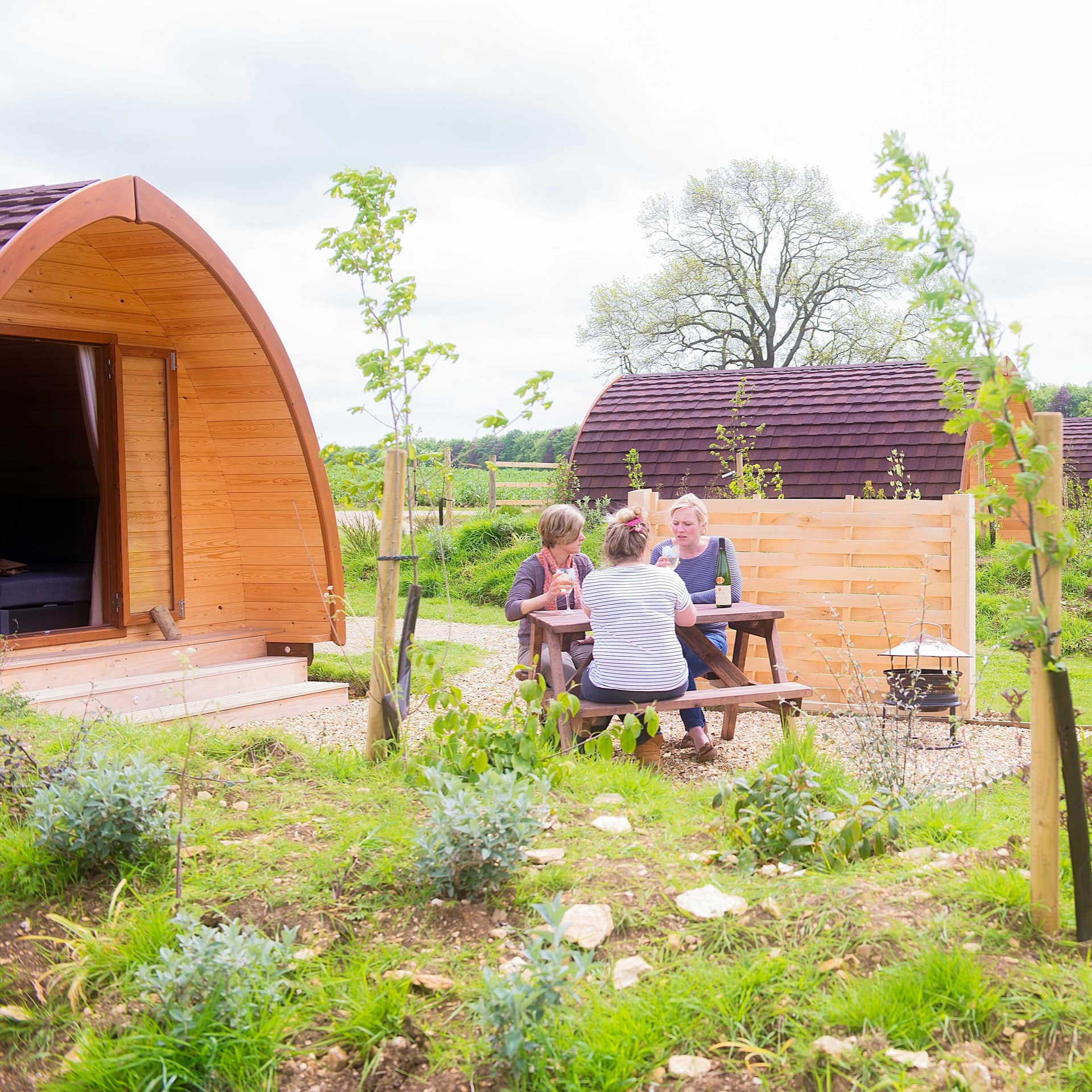 A group of friends enjoy a glass of wine on a picnic table right outside their glamping pod
