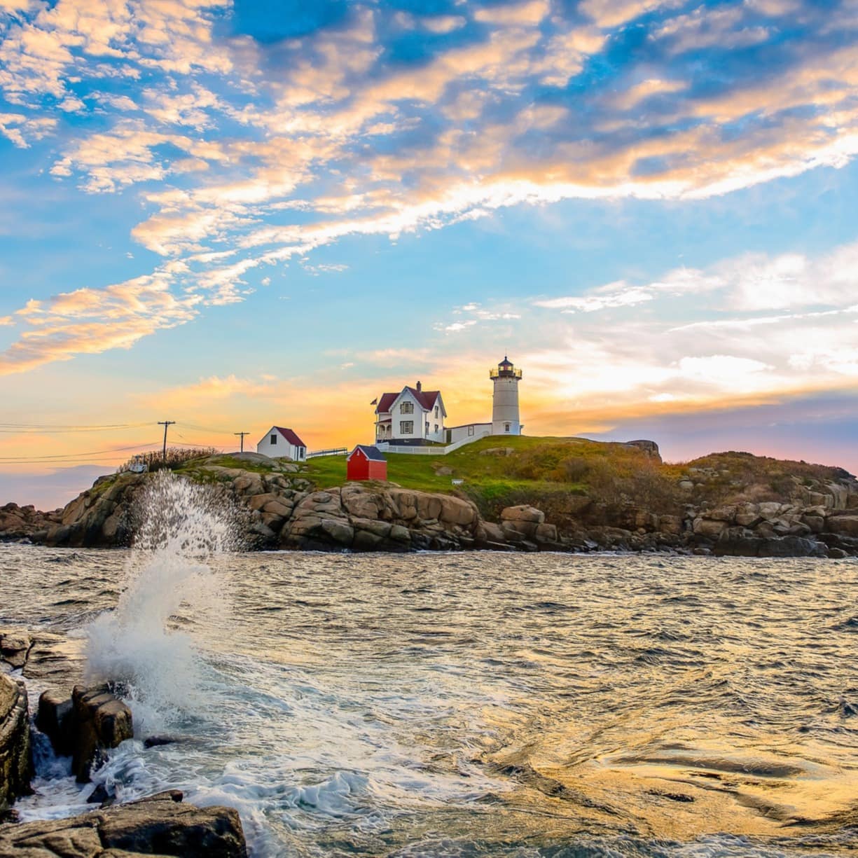 A whitewashed Maine beach house and a lighthouse on a rocky headland