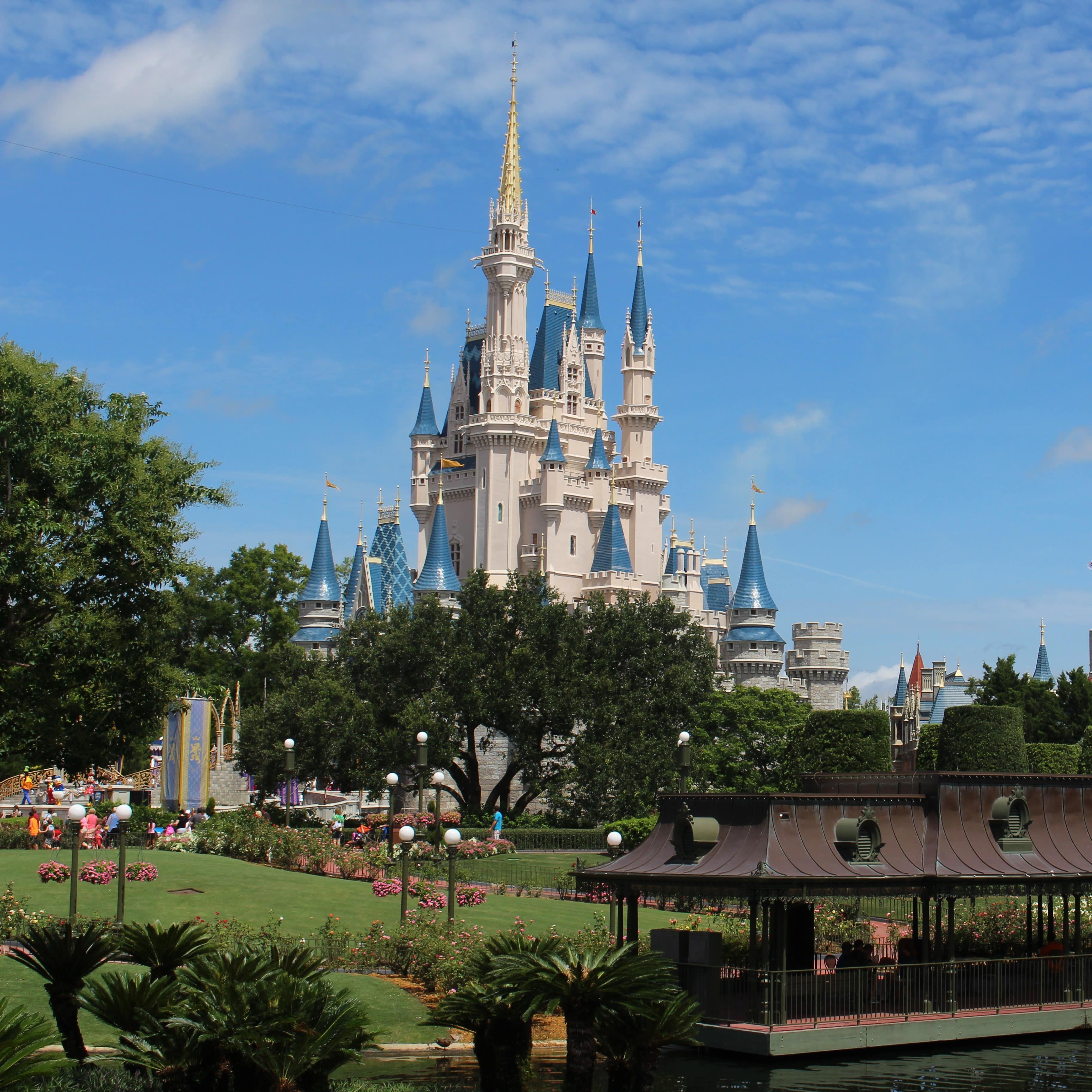 The white-and-blue Cinderella castle with trees and a waterside viewing deck in the foreground