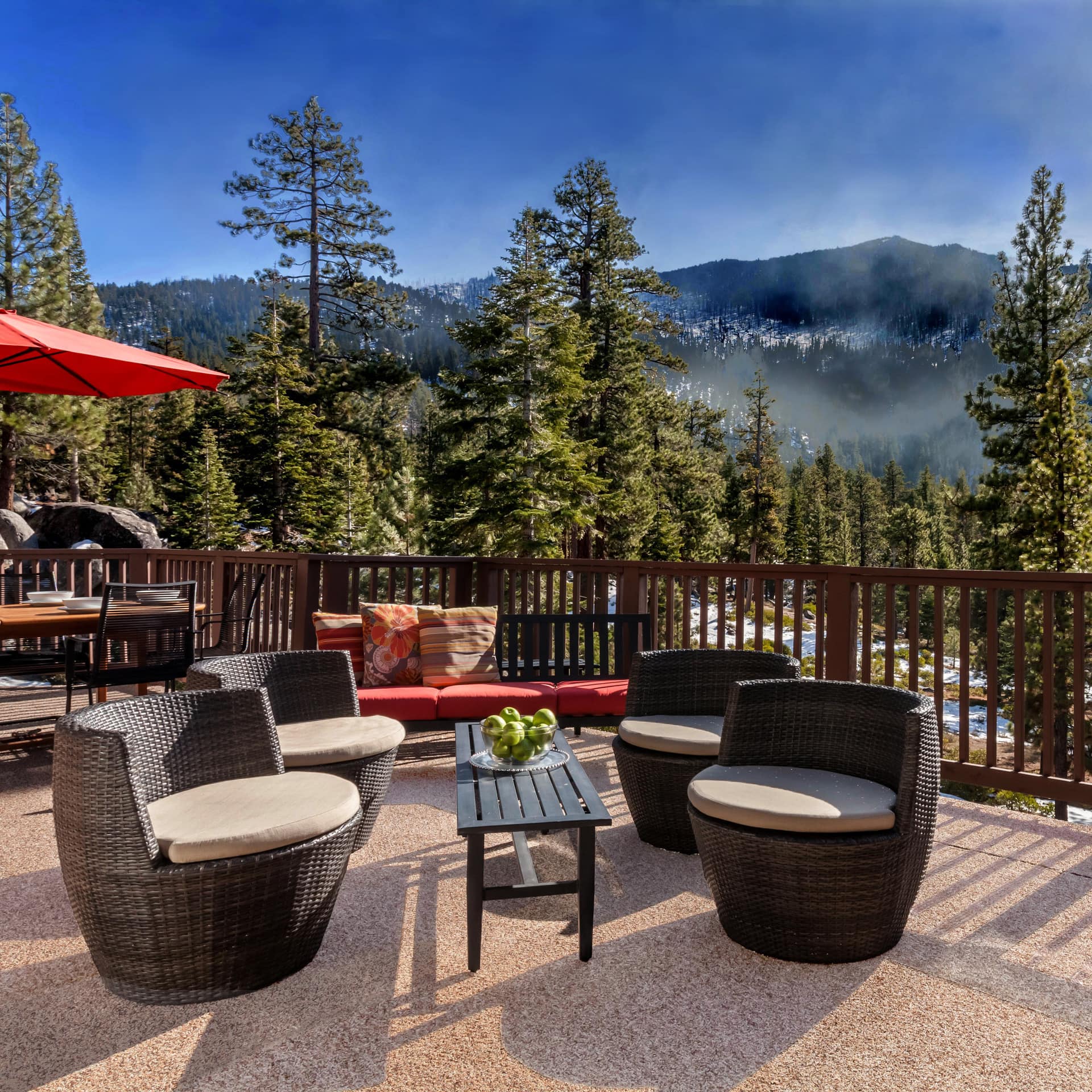 Expansive deck with wicker chairs, tables, and views of forest and mountains