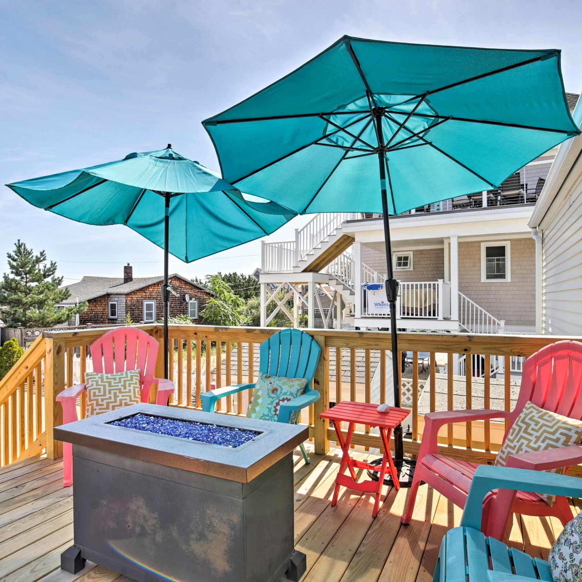 A deck featuring colorful chairs with turquoise umbrellas surrounding a gas firepit