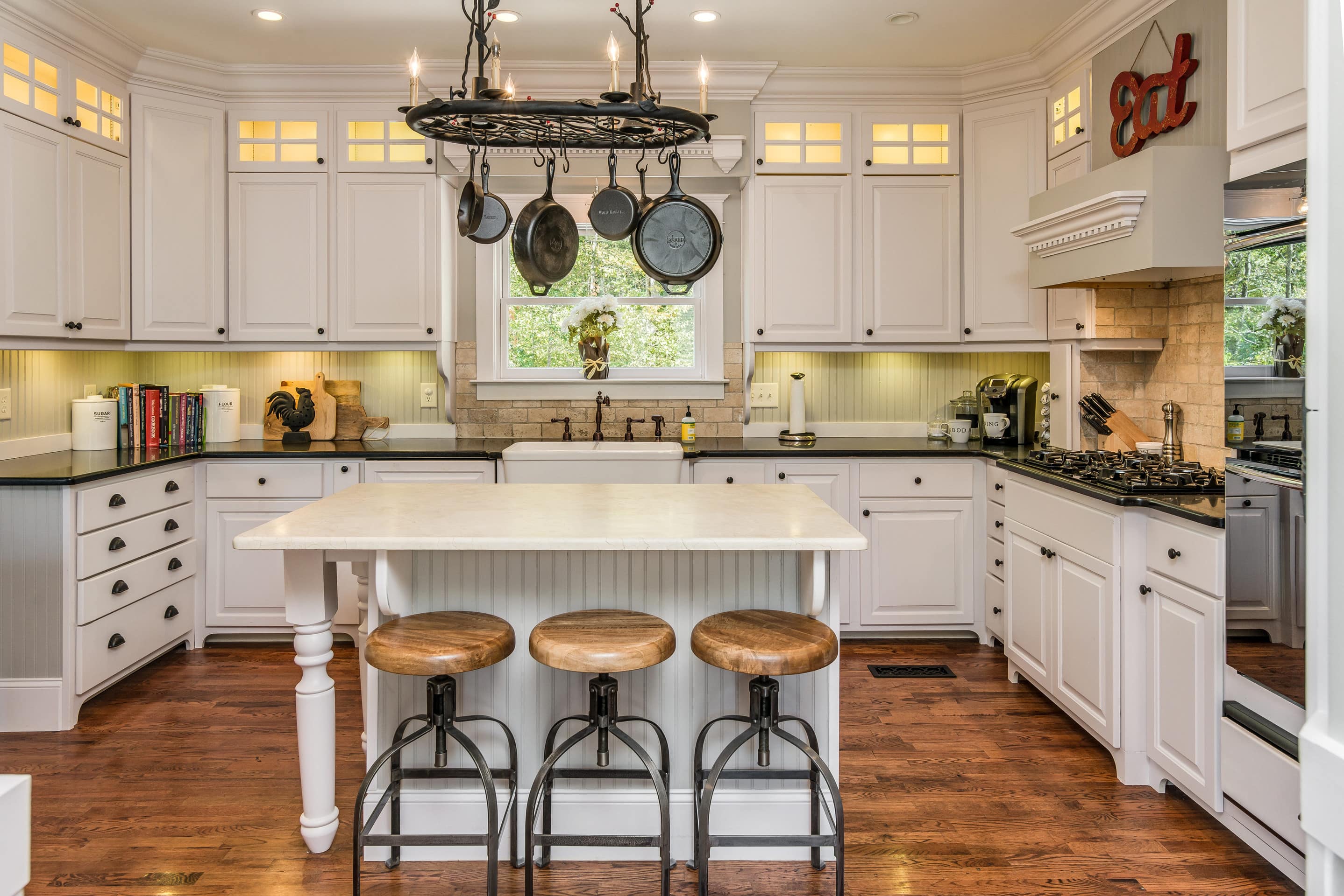 This is a vintage-style kitchen with white cabinets and pots and pans hanging from a ceiling rack.