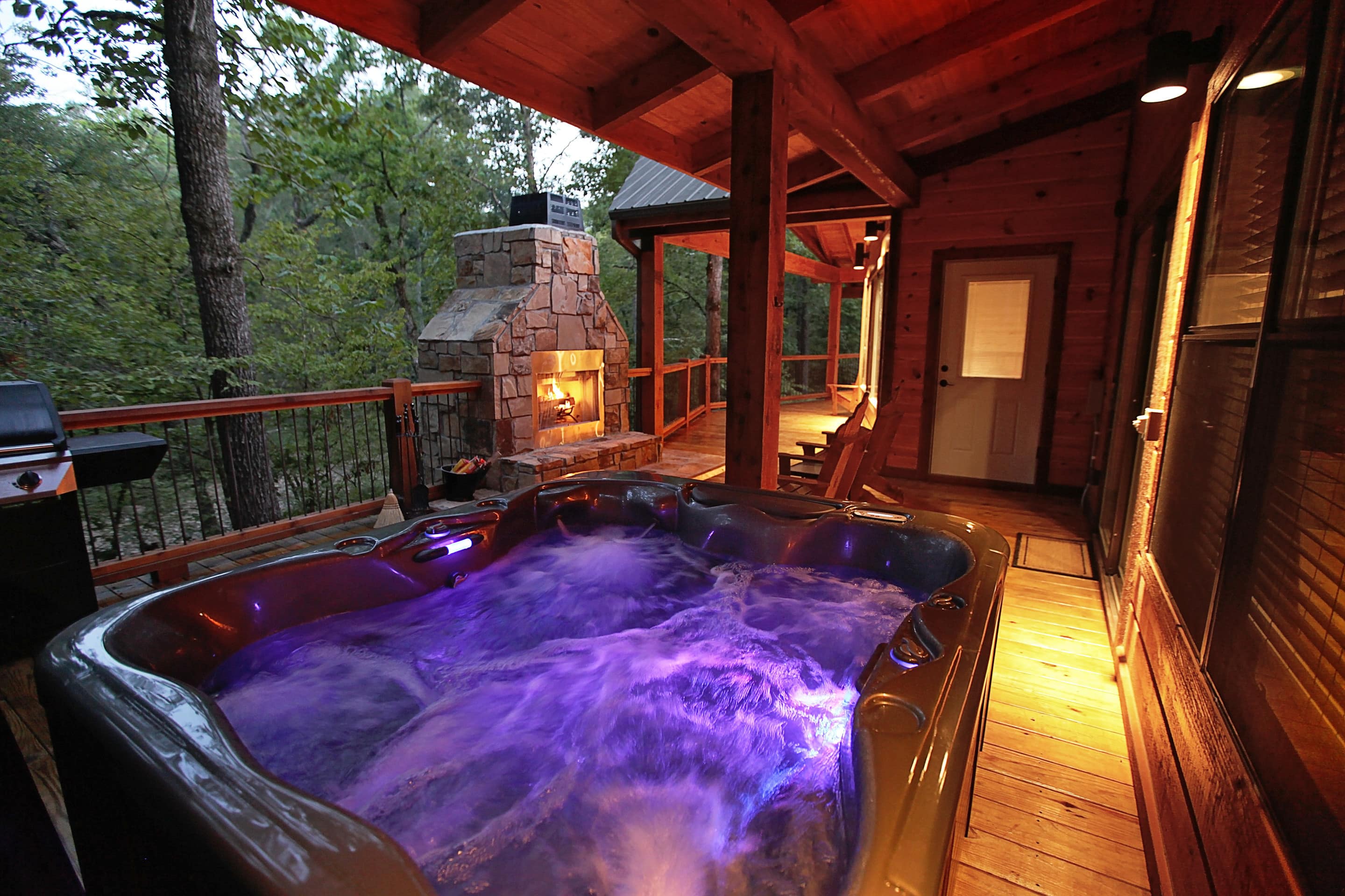 This luxury cabin rental’s outdoor deck features a hot tub, a BBQ grill, and a fireplace.
