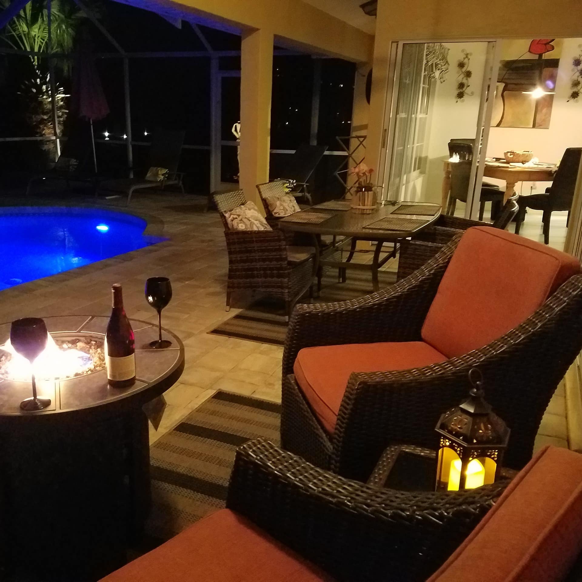 Wicker furniture and a lit fire pit beside the swimming pool of a vacation home rental