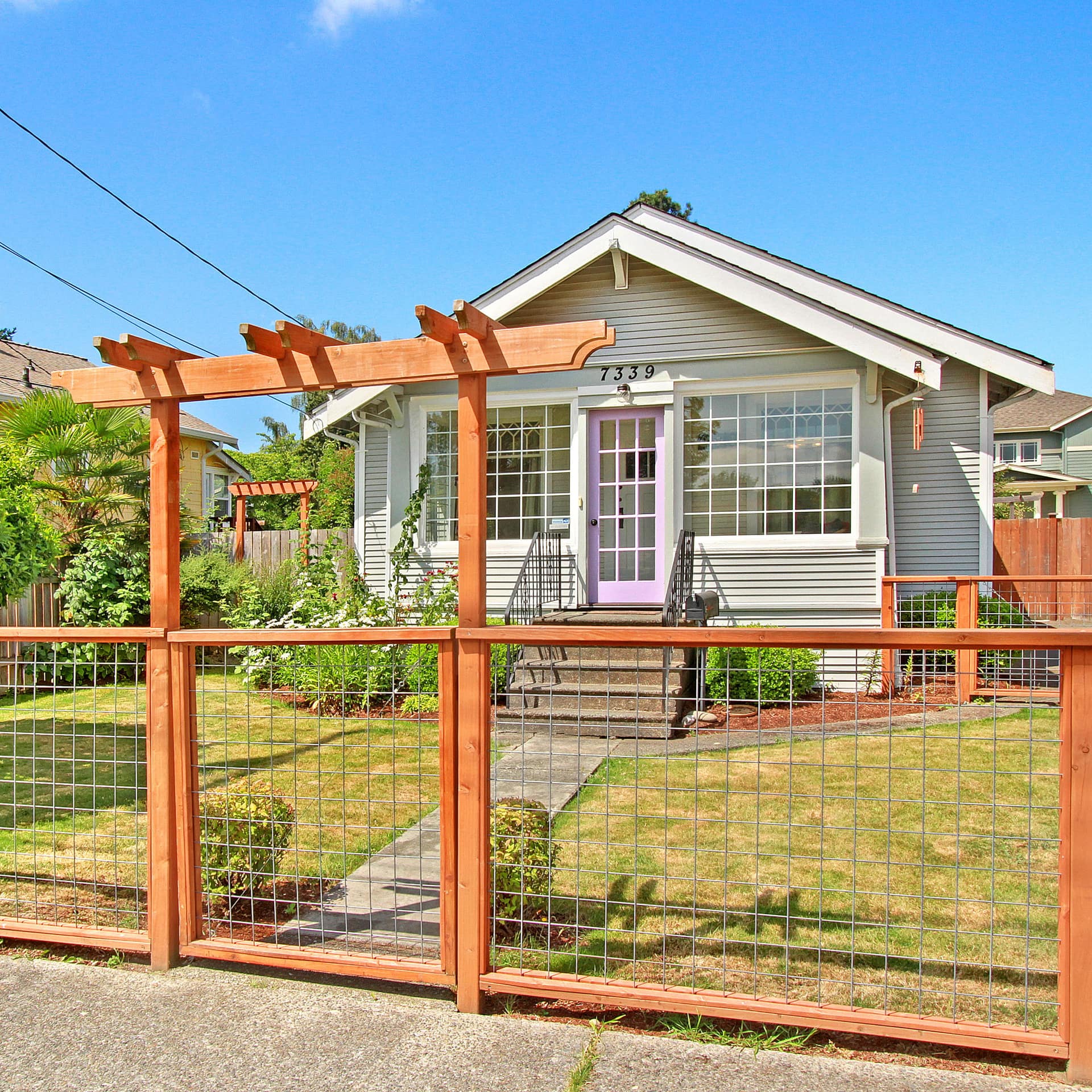 A quaint bungalow with a small lawn and ornamental plants in a fenced front yard