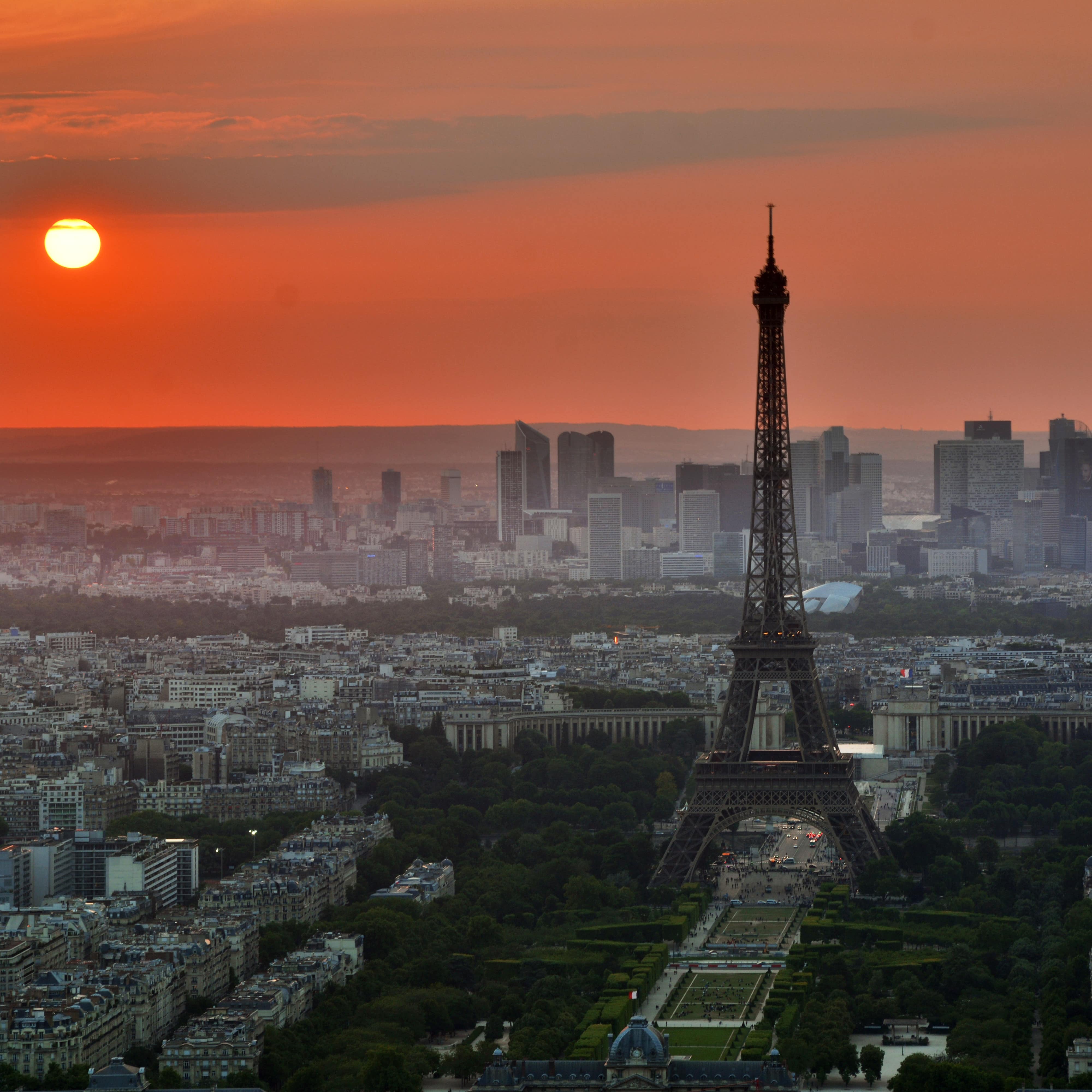 A view of Paris and the Eiffel Tower with skyscrapers of La Defense and the setting sun in the background