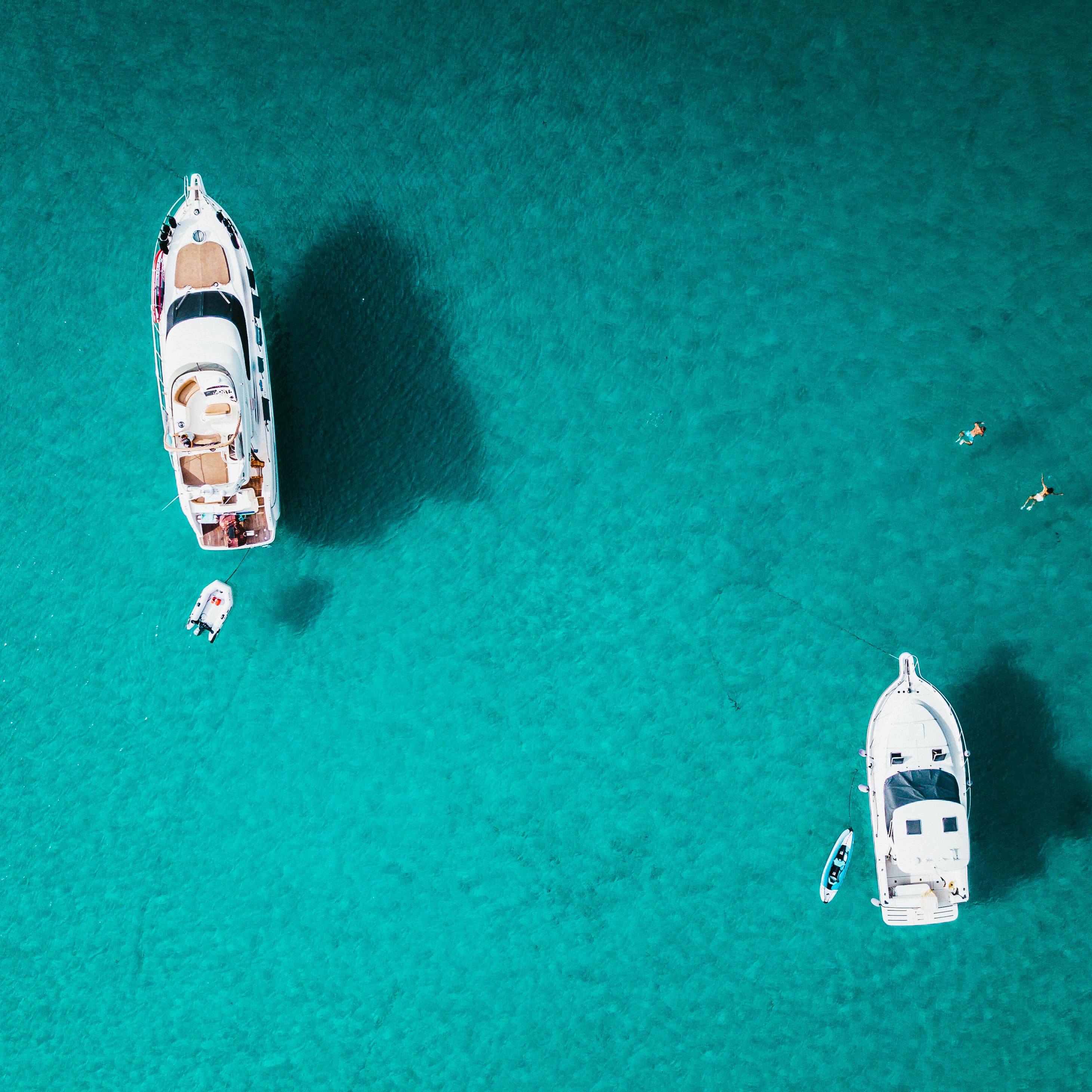 Two boats bob above a turquoise lagoon with people swimming off their sides