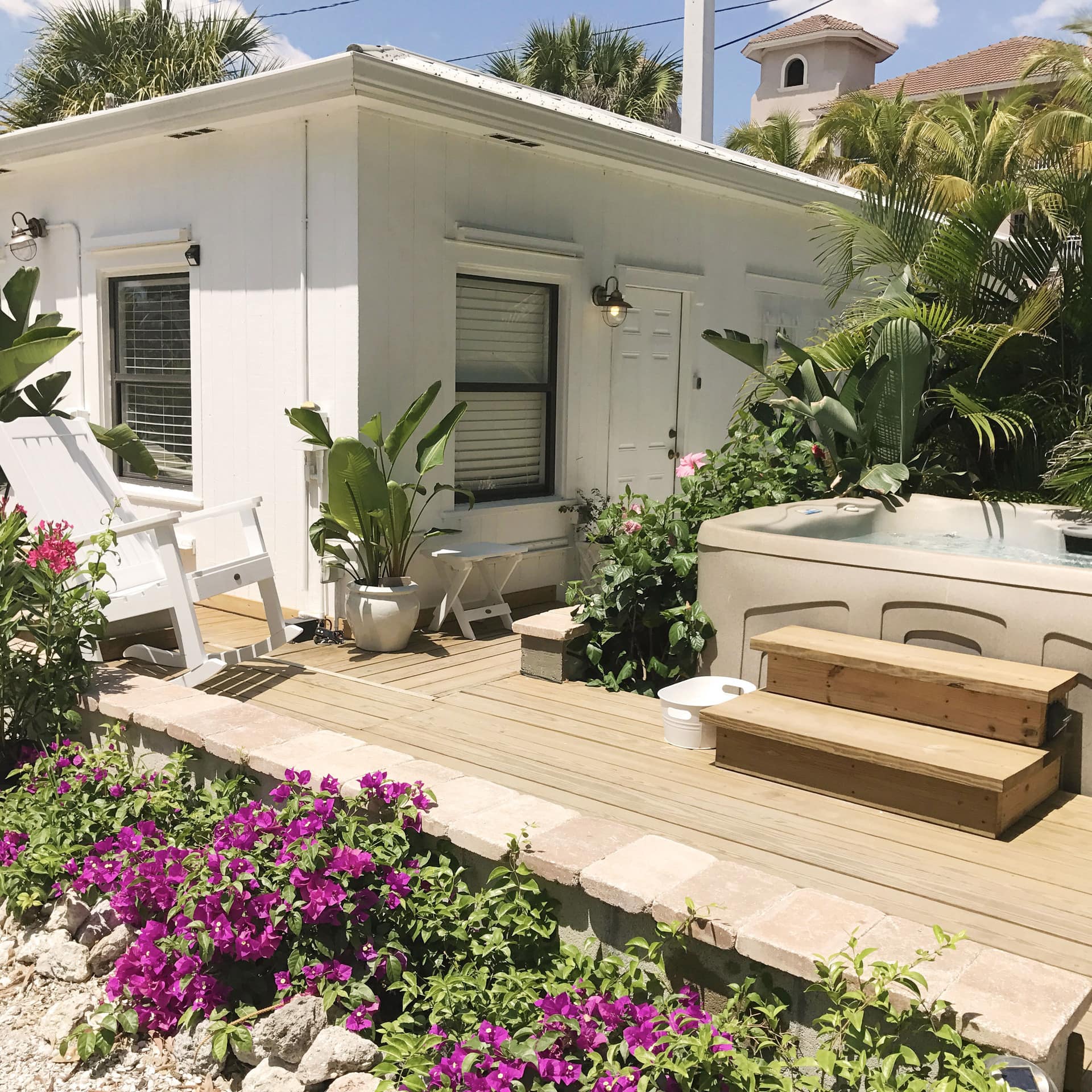 A small white cottage rental with a hot tub and rocking chair on the deck
