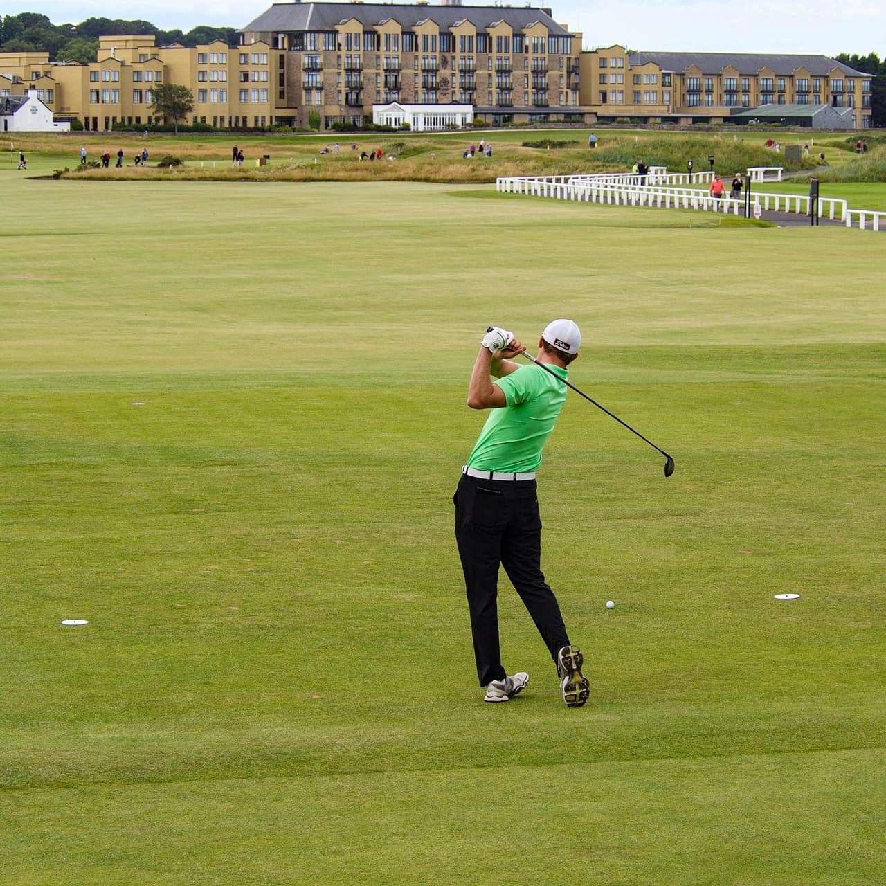 Person swinging a golf club on the fairway with a palatial clubhouse in the background