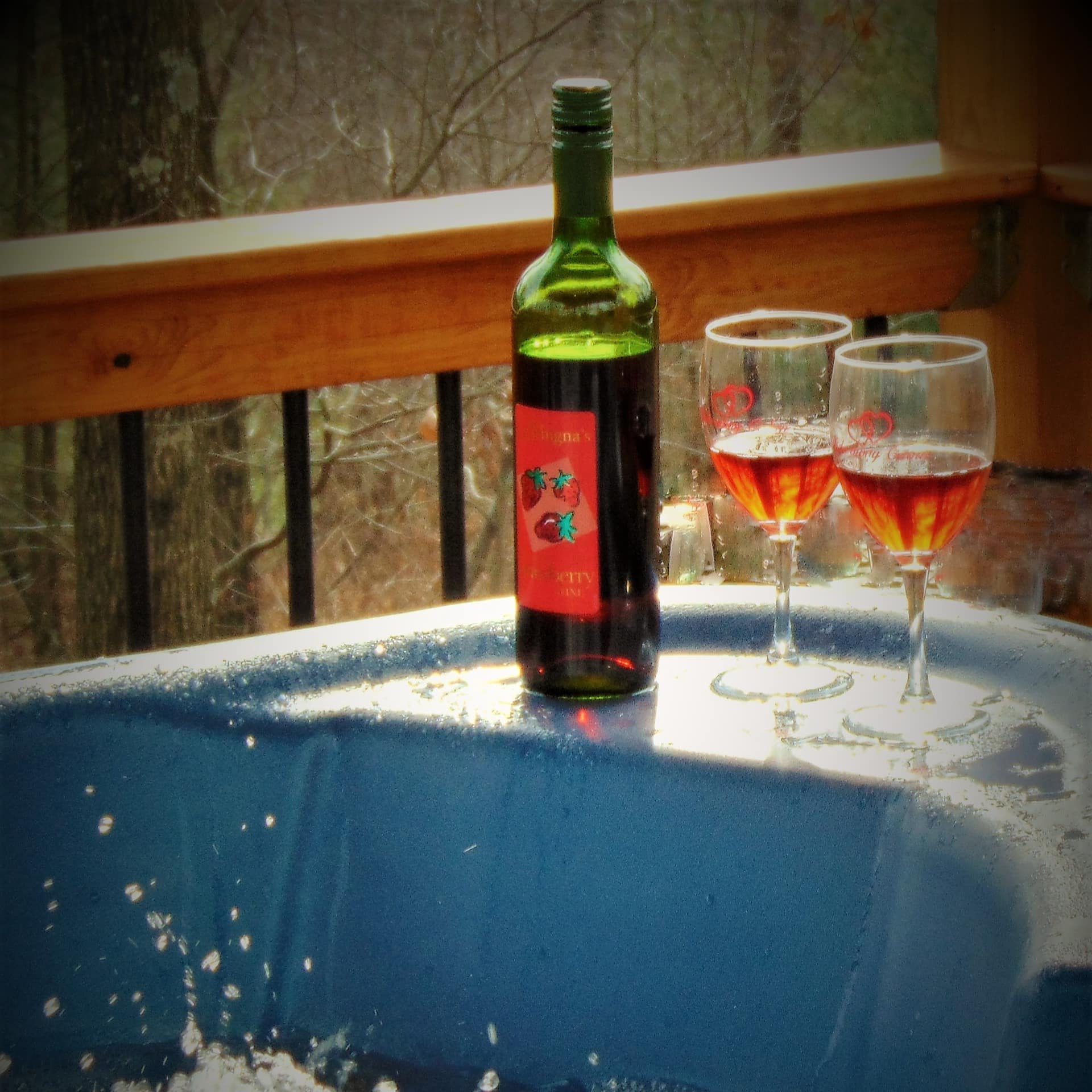 A bottle of wine and 2 glasses by a hot tub on a cabin's deck