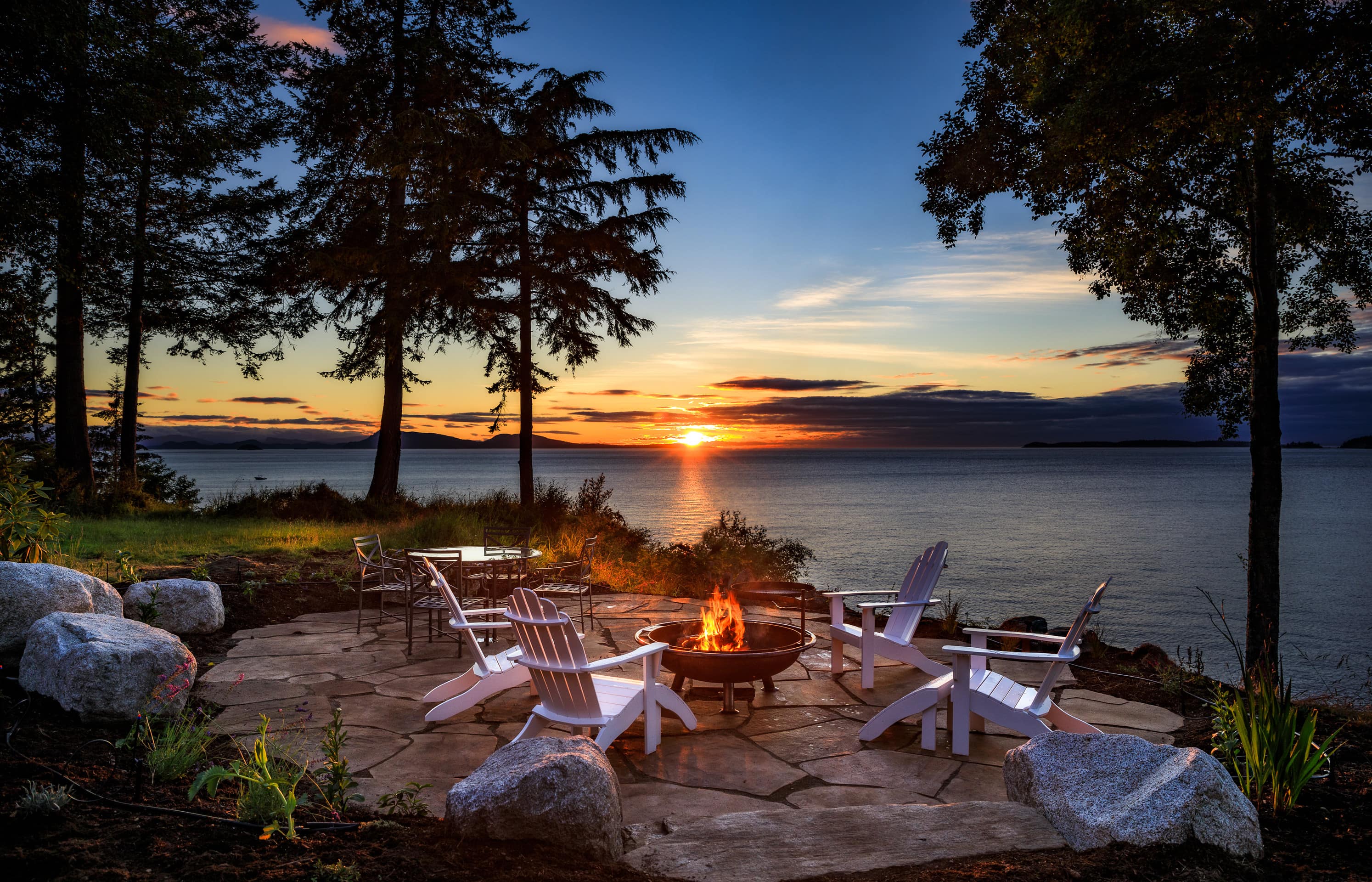 Sunset views from a waterfront cabin rental's patio, which has chairs around a burning fire pit