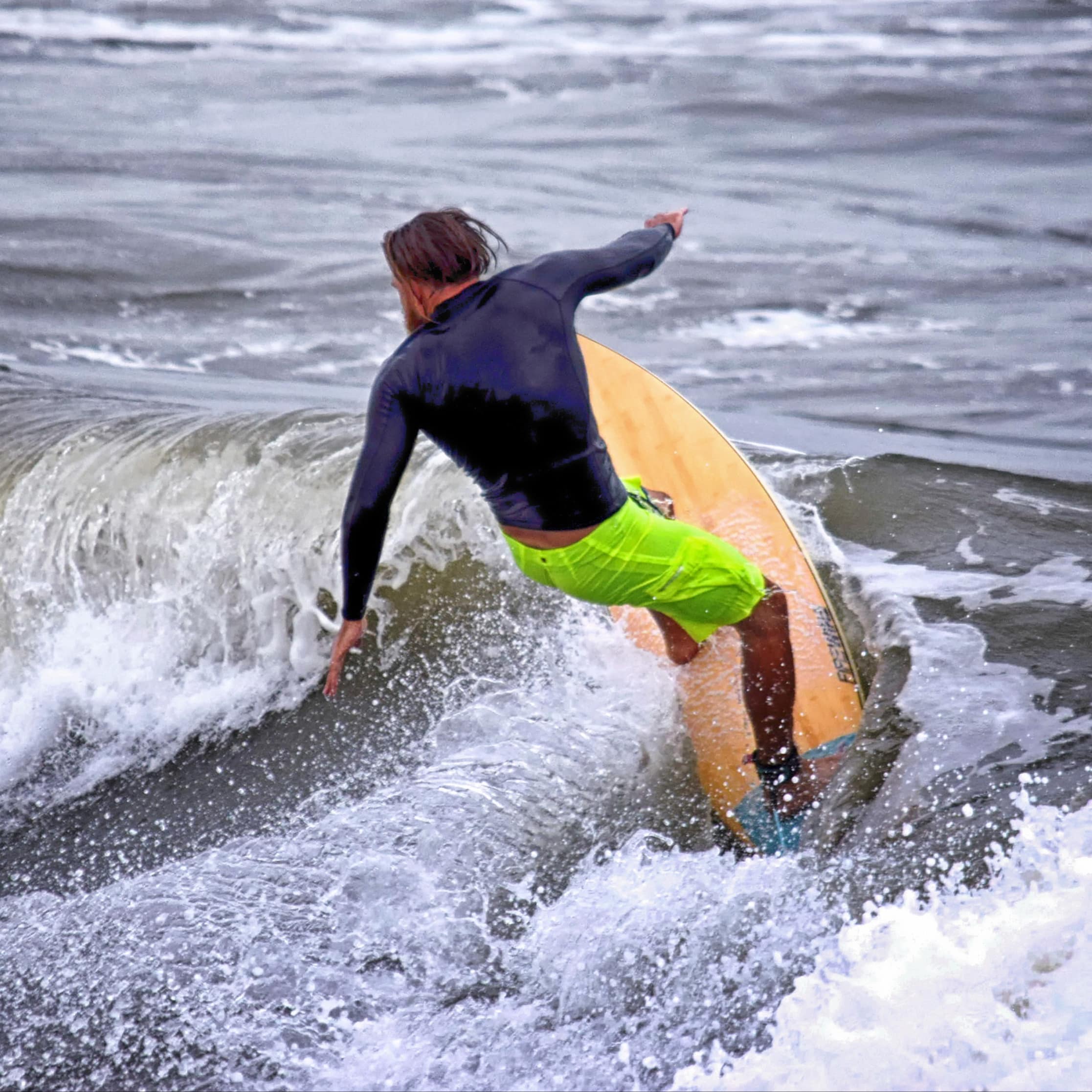 Long-haired man in board shorts surfing a wave just off Atlantic beach