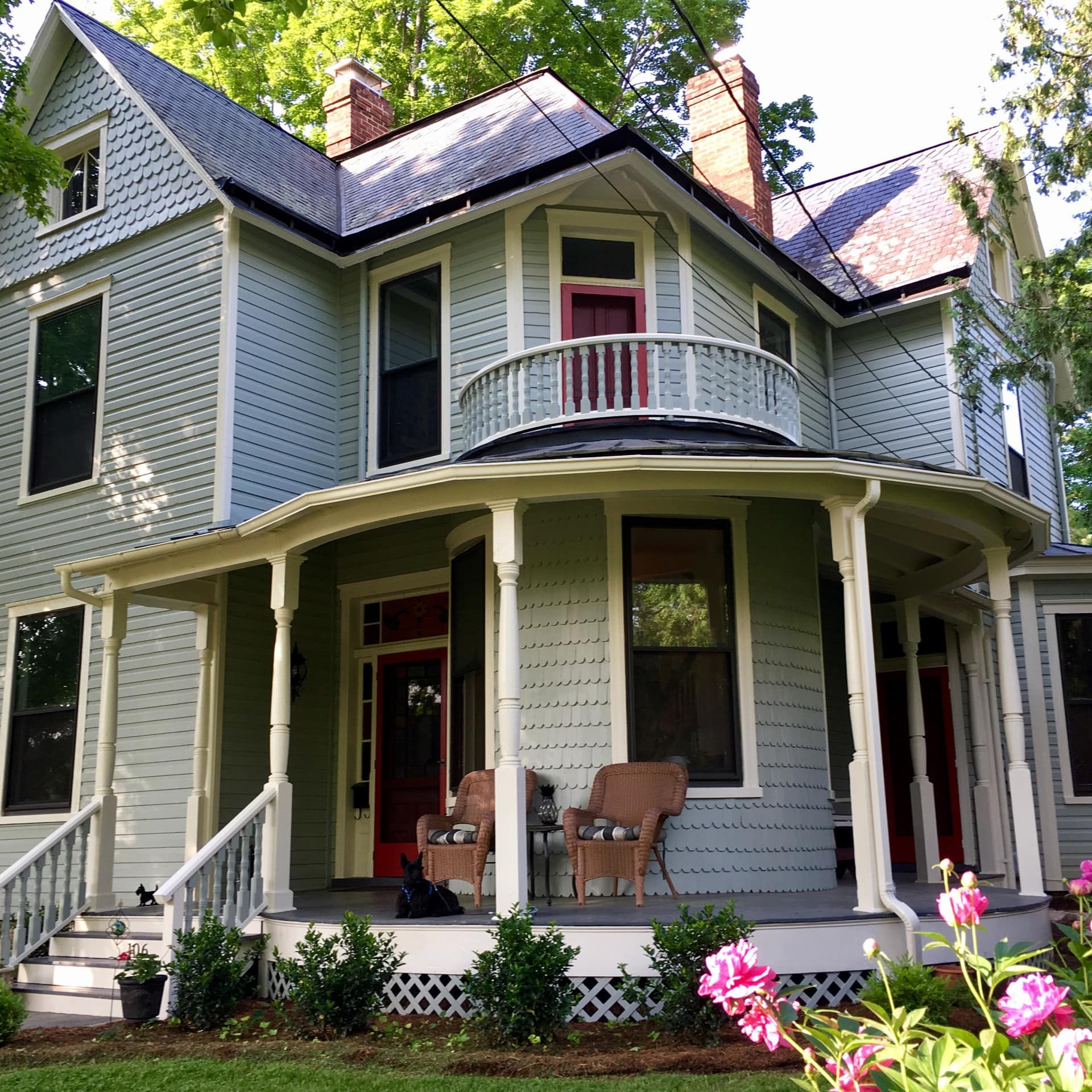 A Victorian-style home in Virginia has a big porch and a garden that has pink flowers