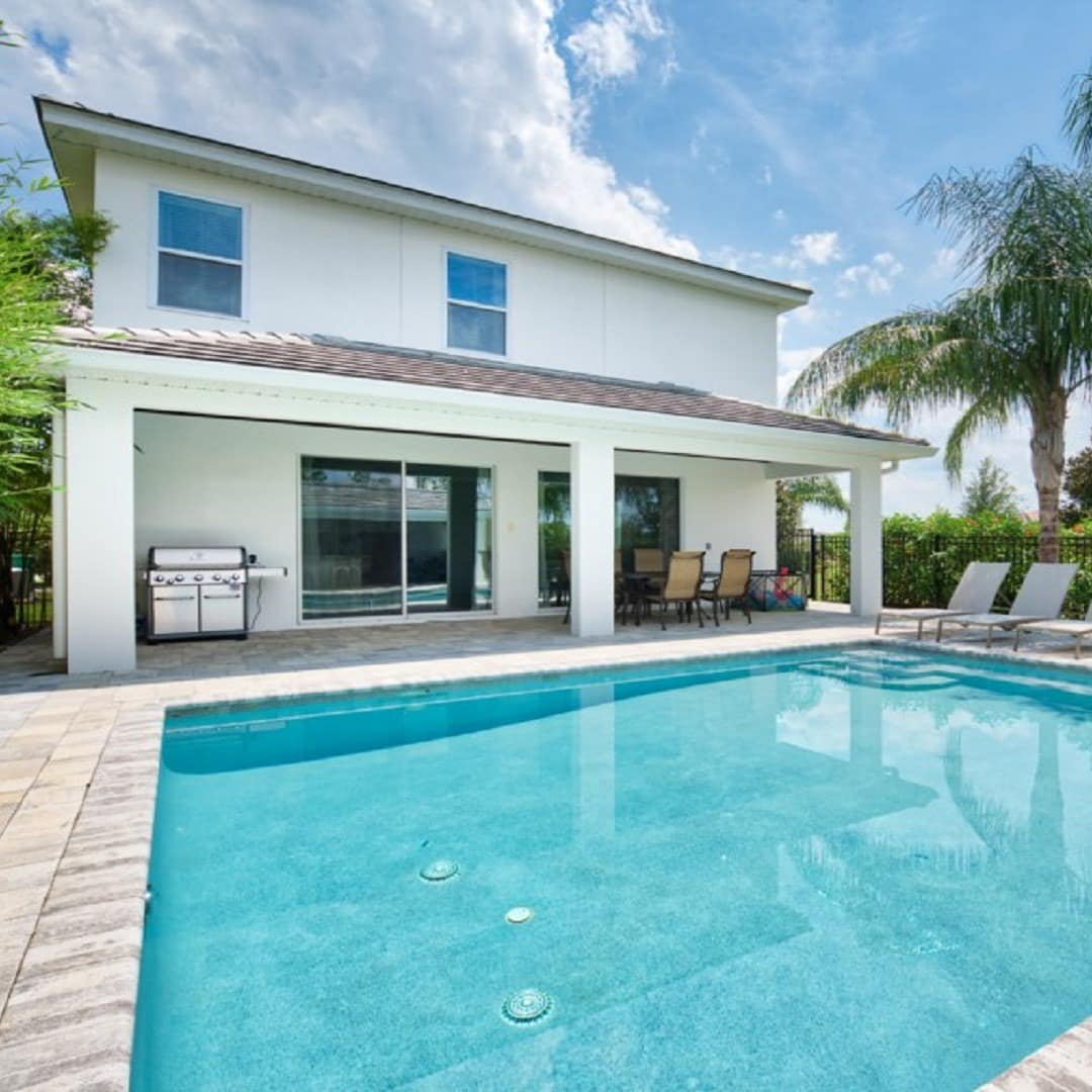 A white villa with a turquoise pool, large barbeque, and seating area in the back