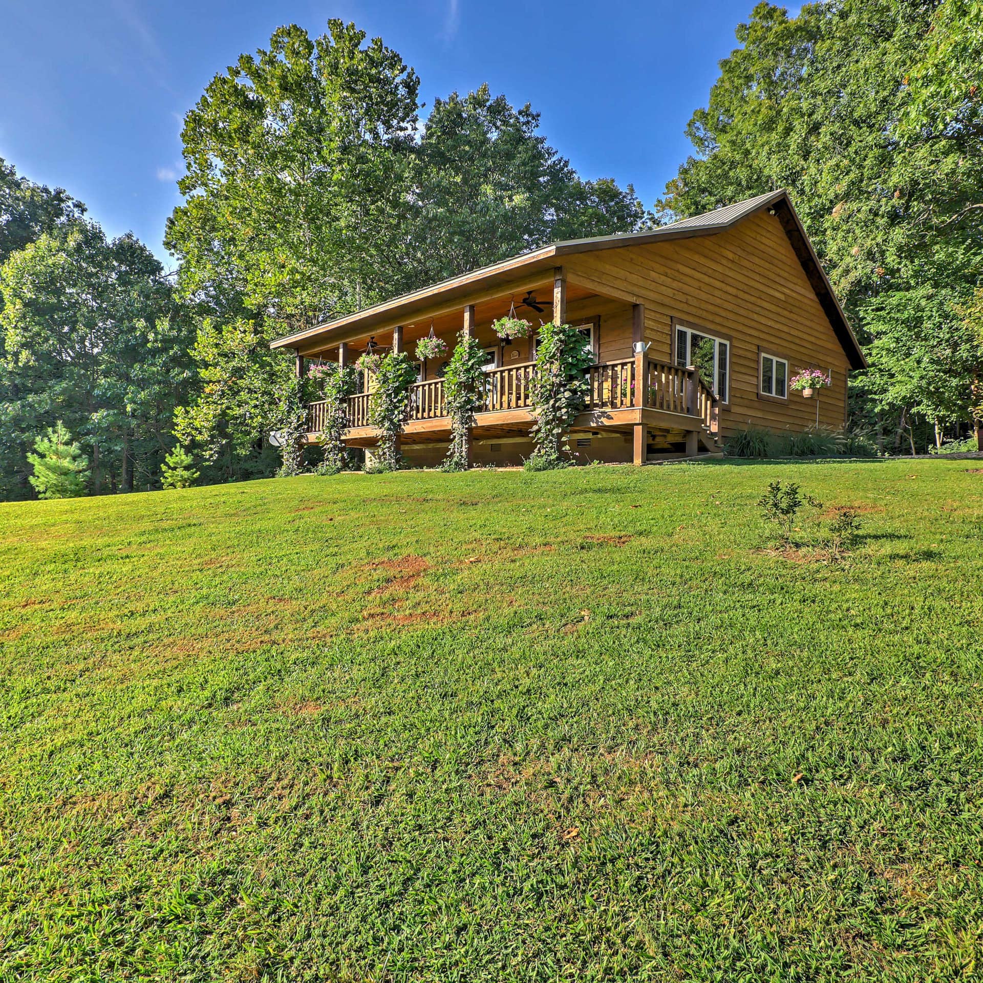 Wooden cabin with an expansive deck, set on a sunny hillside