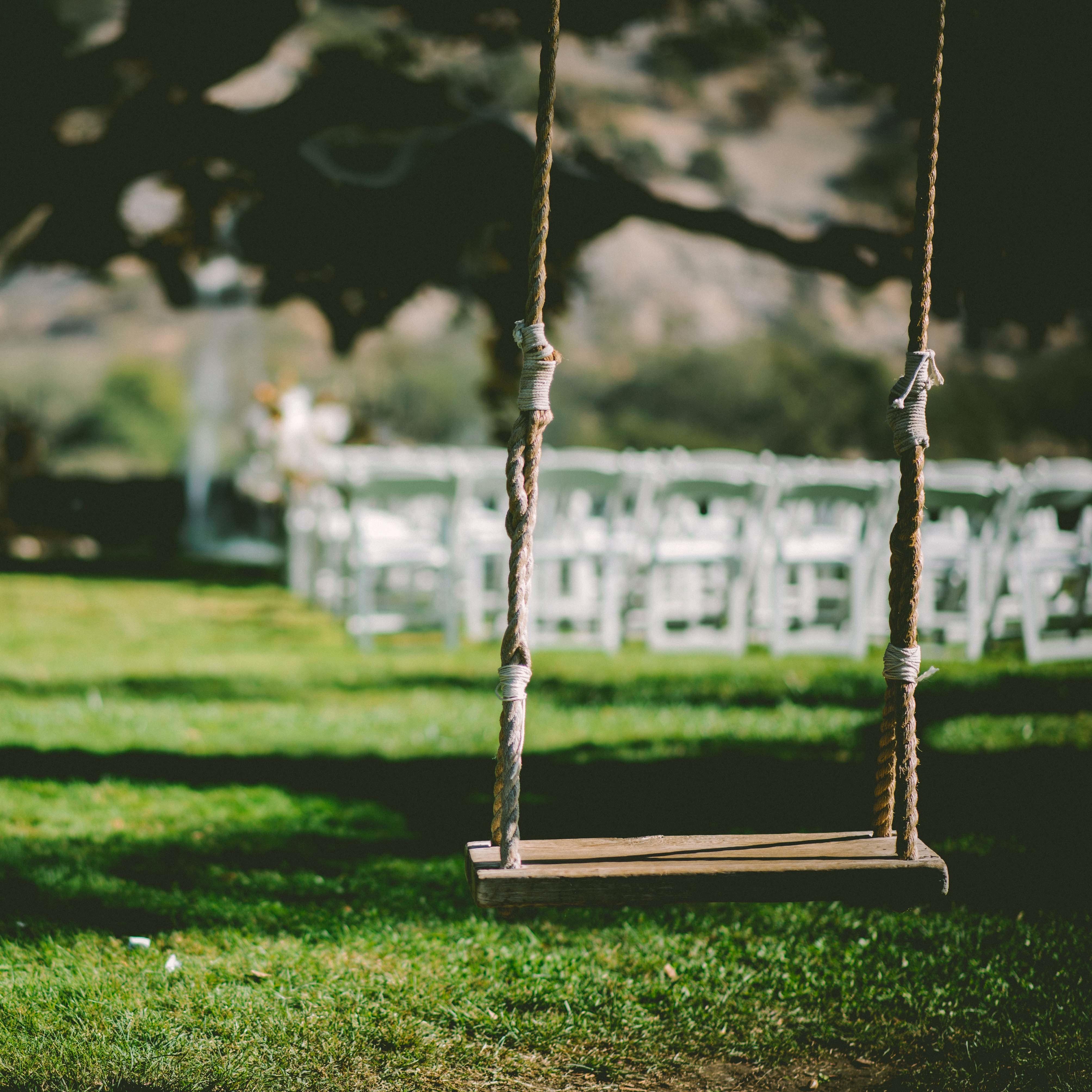 A swing hanging from a tree in a lush backyard, with seats for a wedding ceremony set up in the background